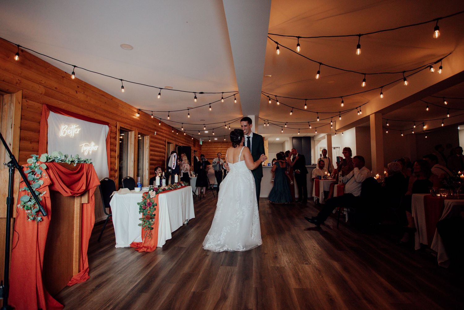 Wedding reception venue with wooden walls, string lights, and dance floor setup.