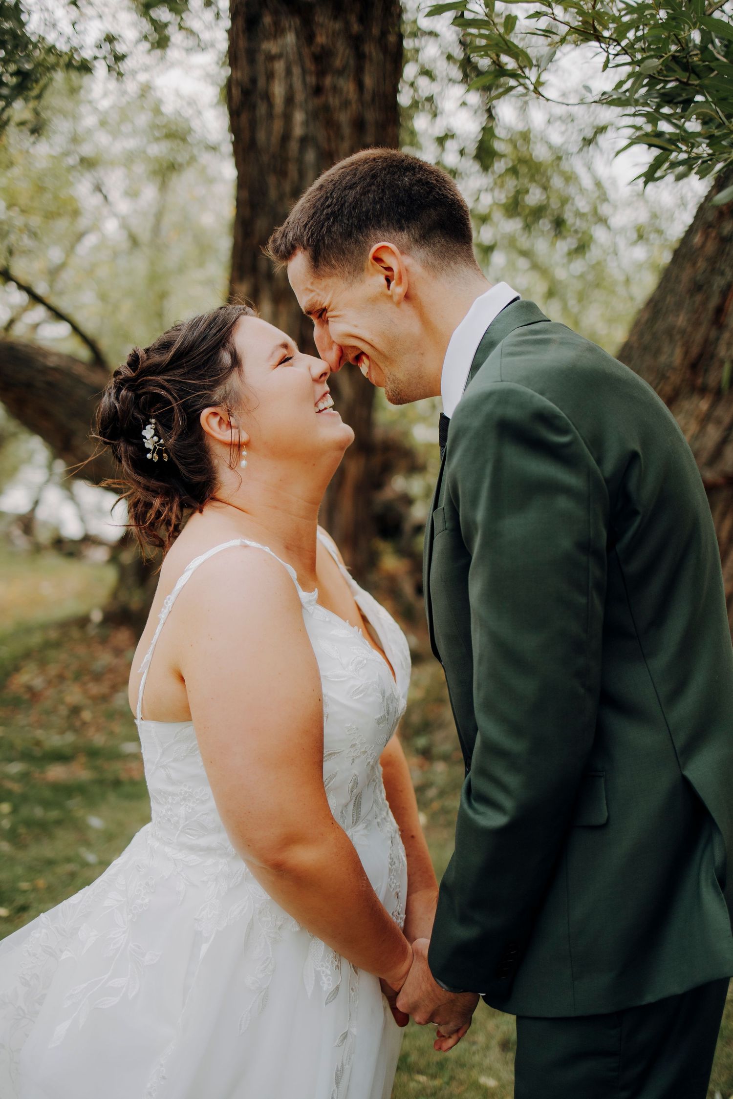 A romantic wedding moment captured outdoors with a couple in white dress and dark green suit.