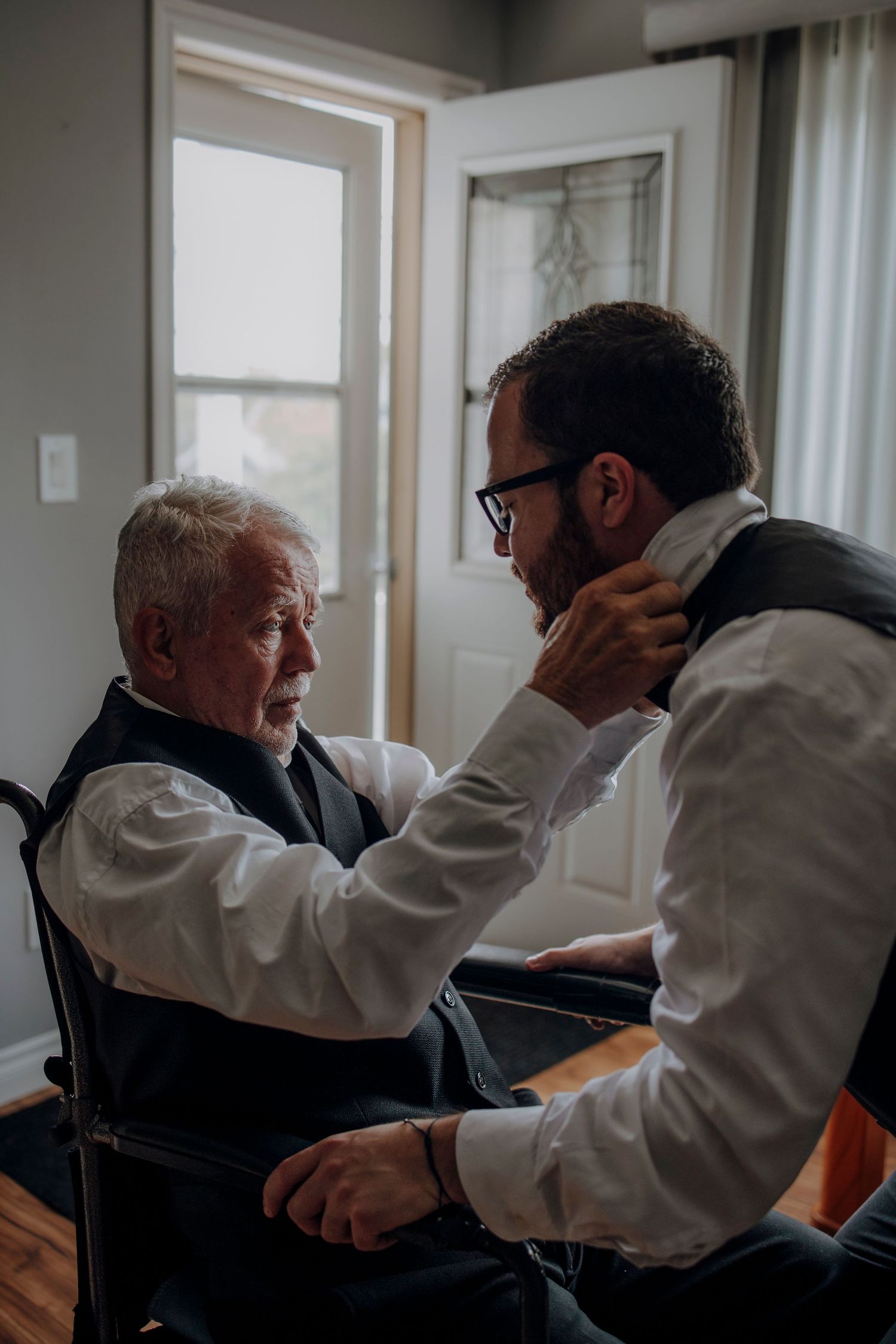 Healthcare worker in white coat provides care to elderly patient in dark clothing at home.
