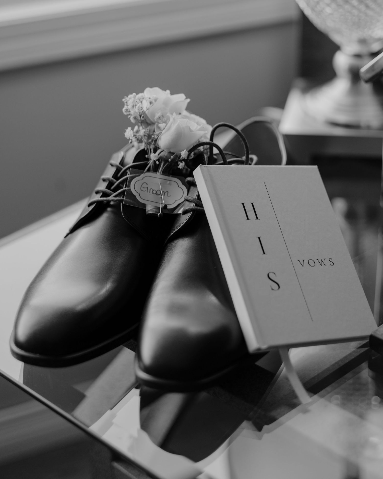 Black dress shoes and wedding vows displayed on a table in black and white.