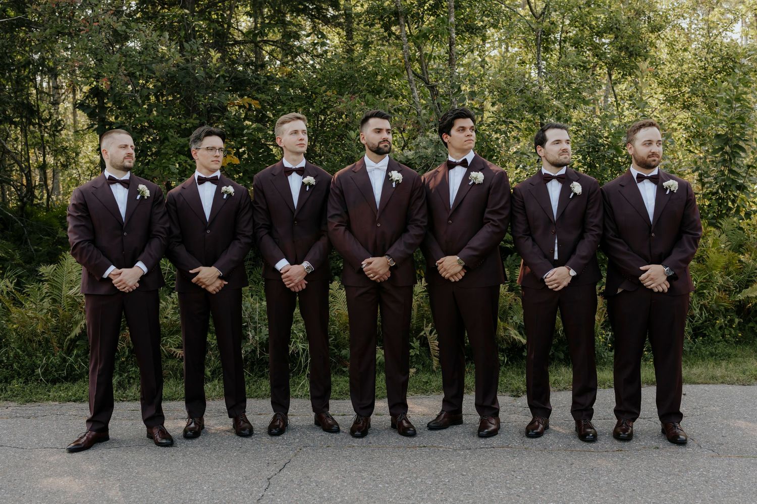 Groomsmen in dark suits lined up outdoors for formal wedding party photo.