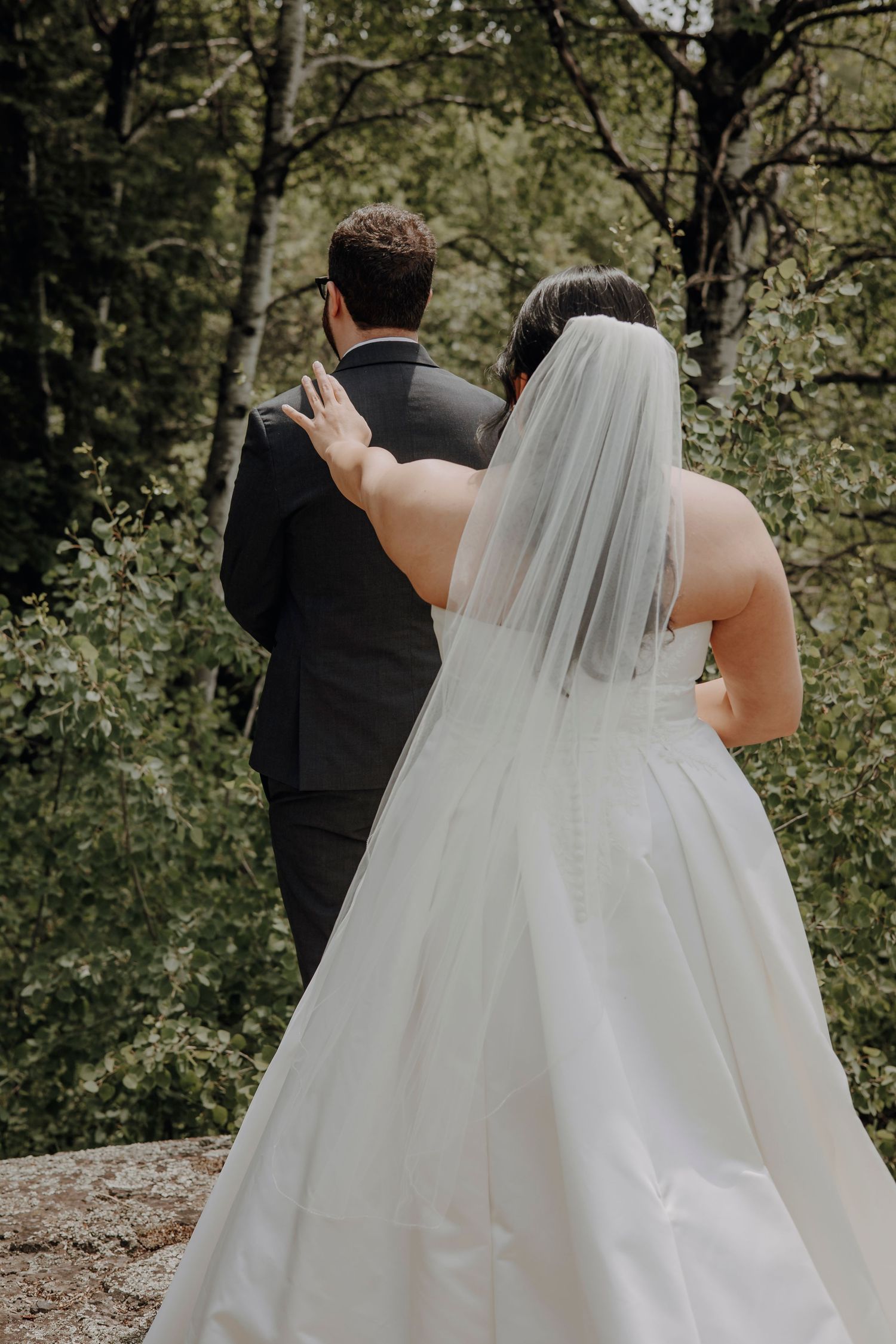 Wedding couple walking through wooded area with bride wearing flowing white dress and veil.