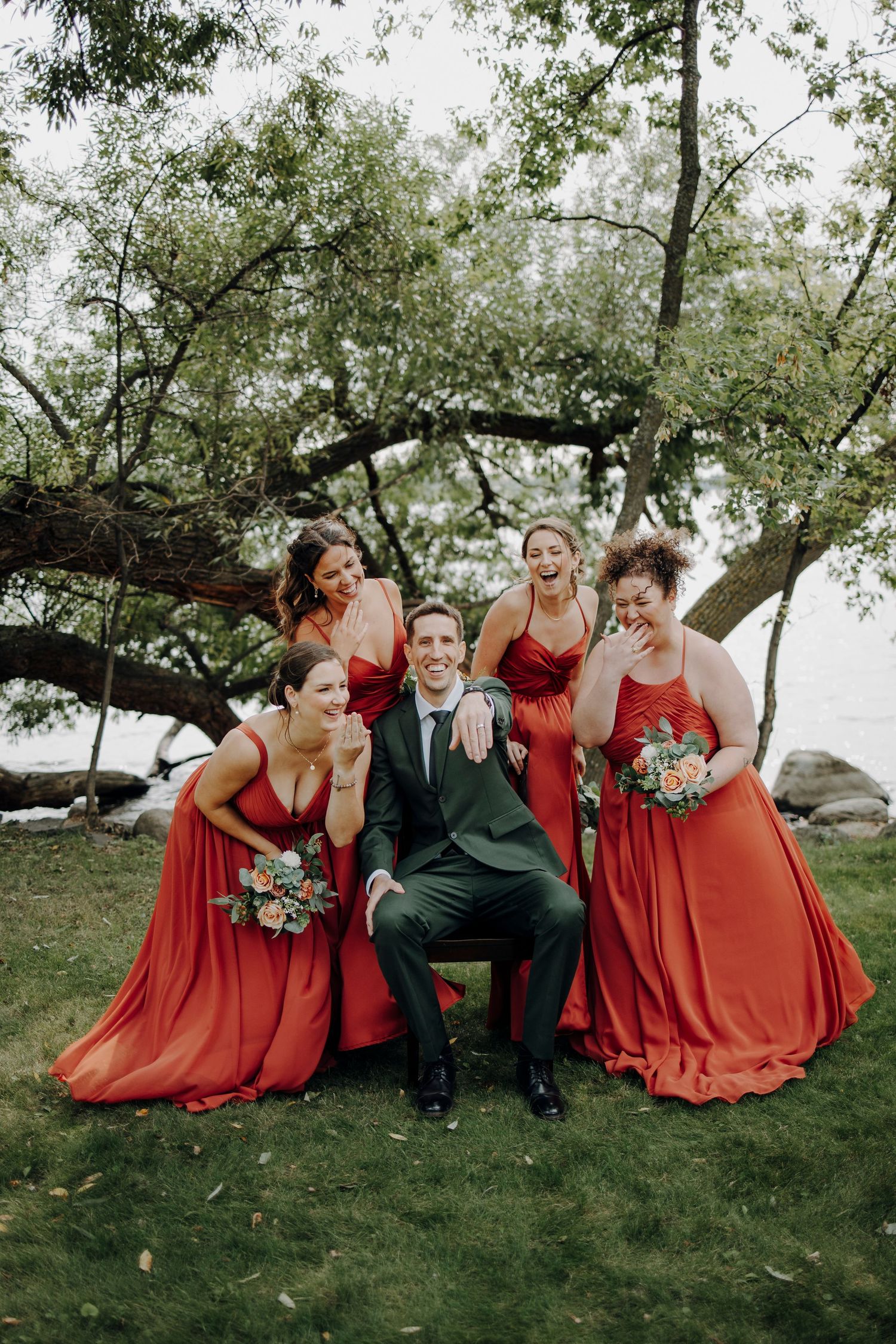Wedding party relaxing on grass wearing burgundy dresses and suits.