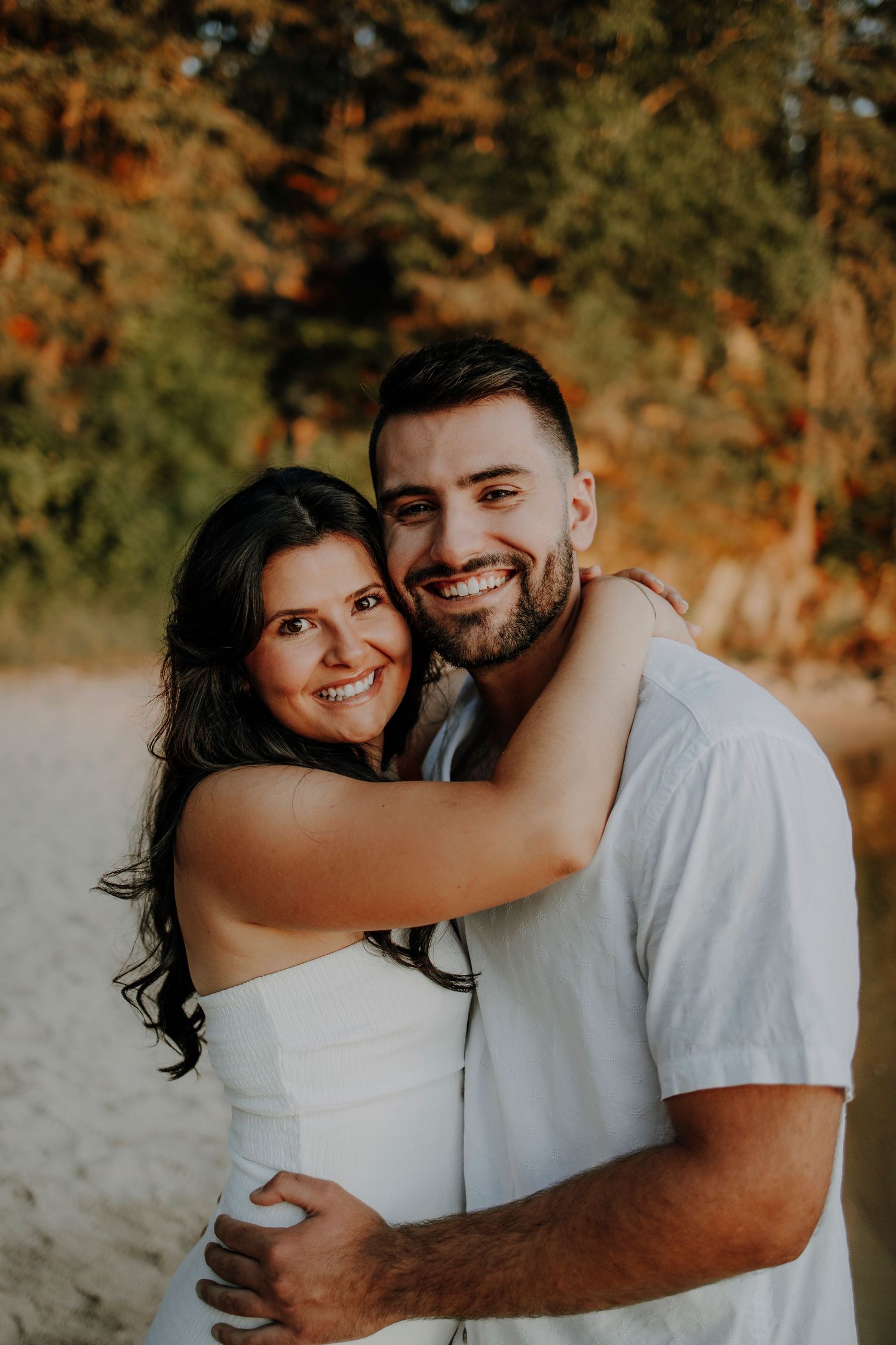 A joyful embrace captured on a beach during golden hour with warm autumn colors.