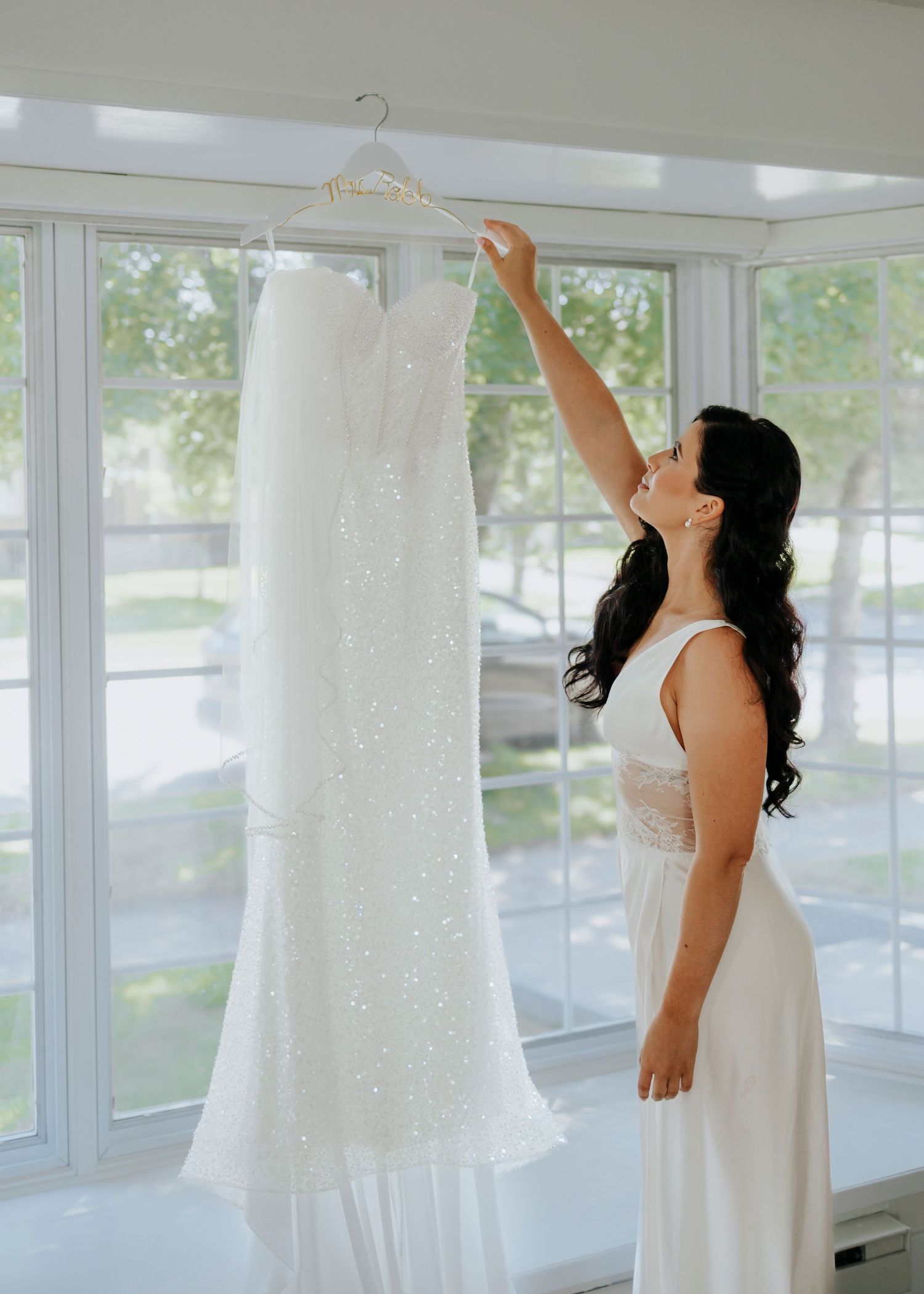 White wedding dresses hanging in a bright sunlit room with large windows.