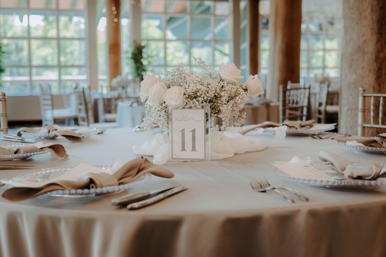 An elegant wedding reception table setting with natural light streaming through large windows.