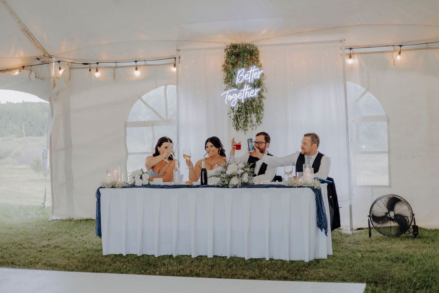 White wedding reception tent setup with elegant table arrangements and string lighting.