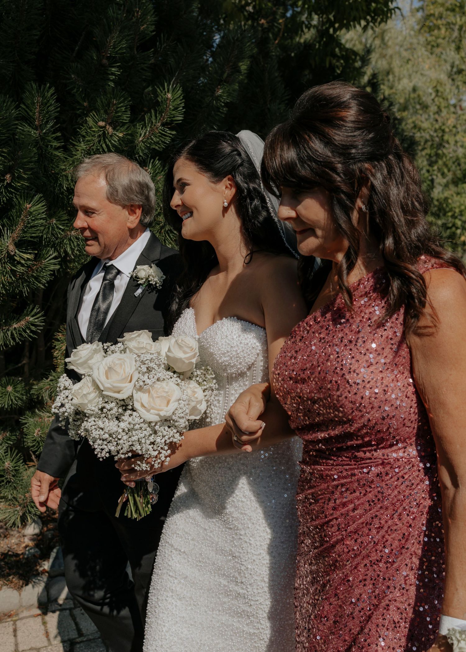 Wedding party members pose together outdoors with white floral bouquets.