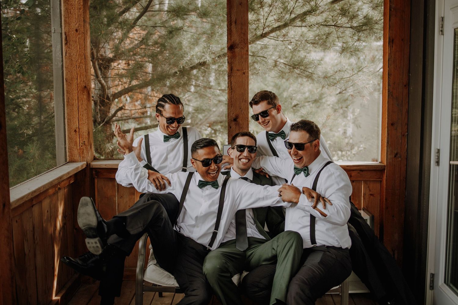 Groomsmen in gray suits and sunglasses pose together in a fun group photo against a light background.