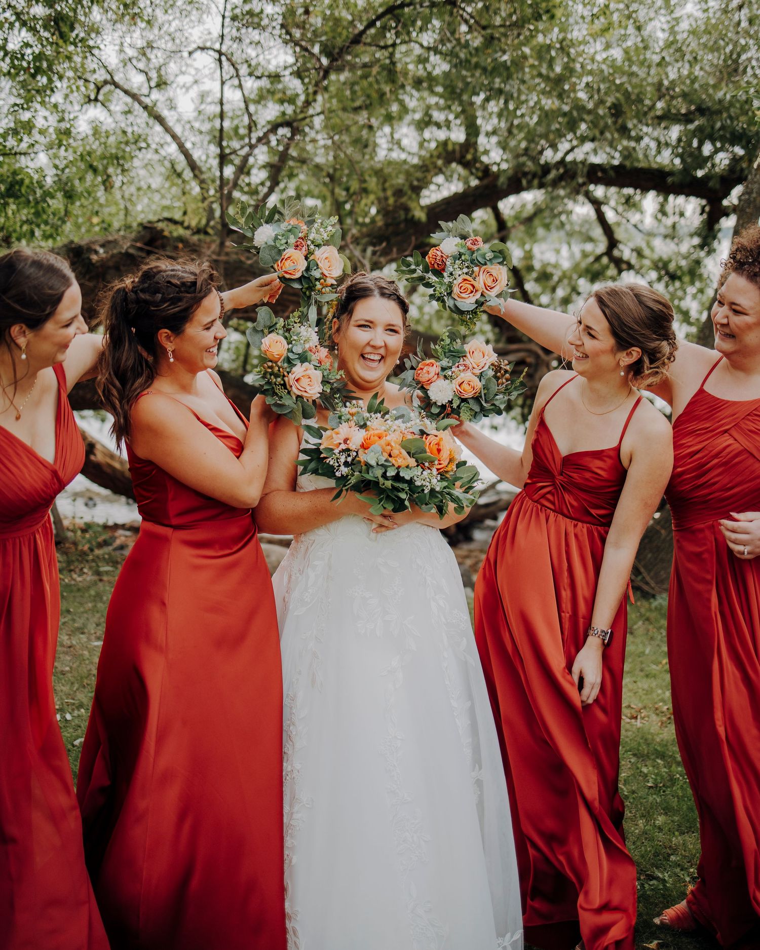 Bridesmaids in red dresses celebrating with bride in white gown outdoors.