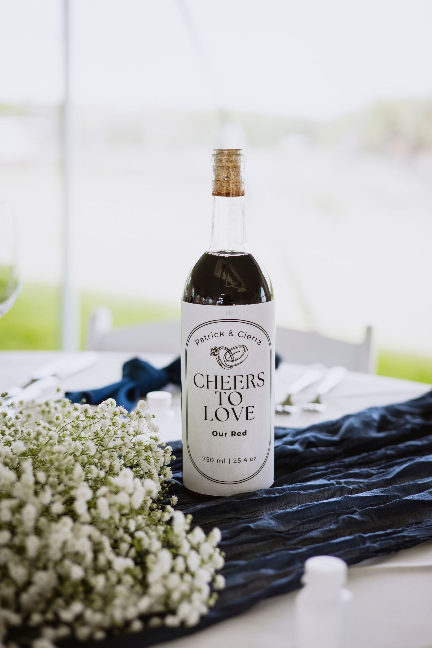 Wedding decor featuring bottles labeled 'Love' and 'Cheers' with baby's breath flowers on navy blue fabric.