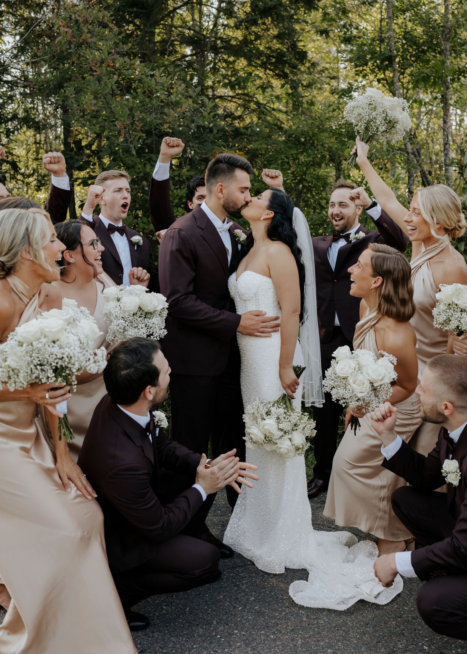 Wedding party celebrates with joy during outdoor ceremony as newlyweds share romantic moment surrounded by white flowers.