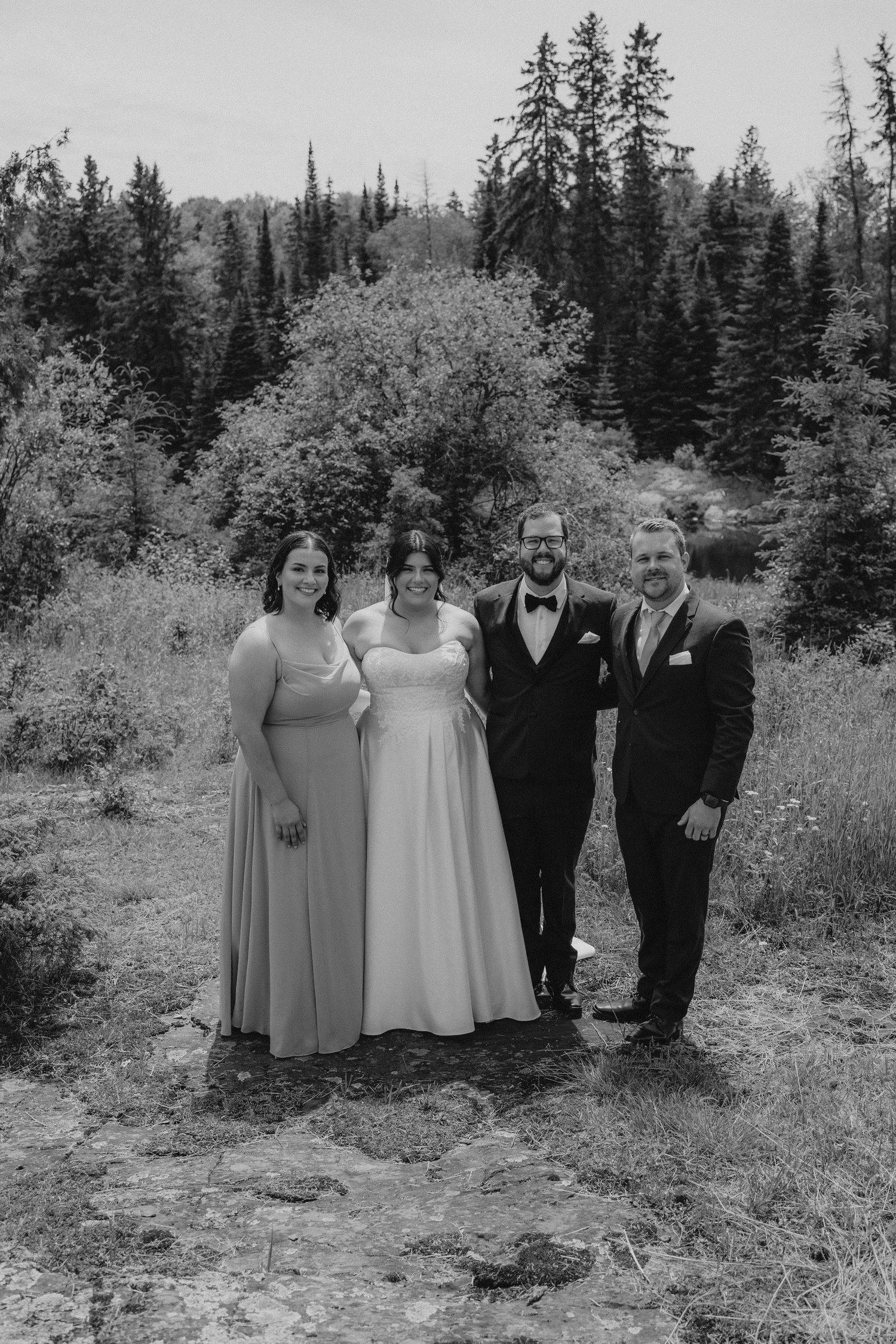 Wedding party poses together outdoors with evergreen trees in background.