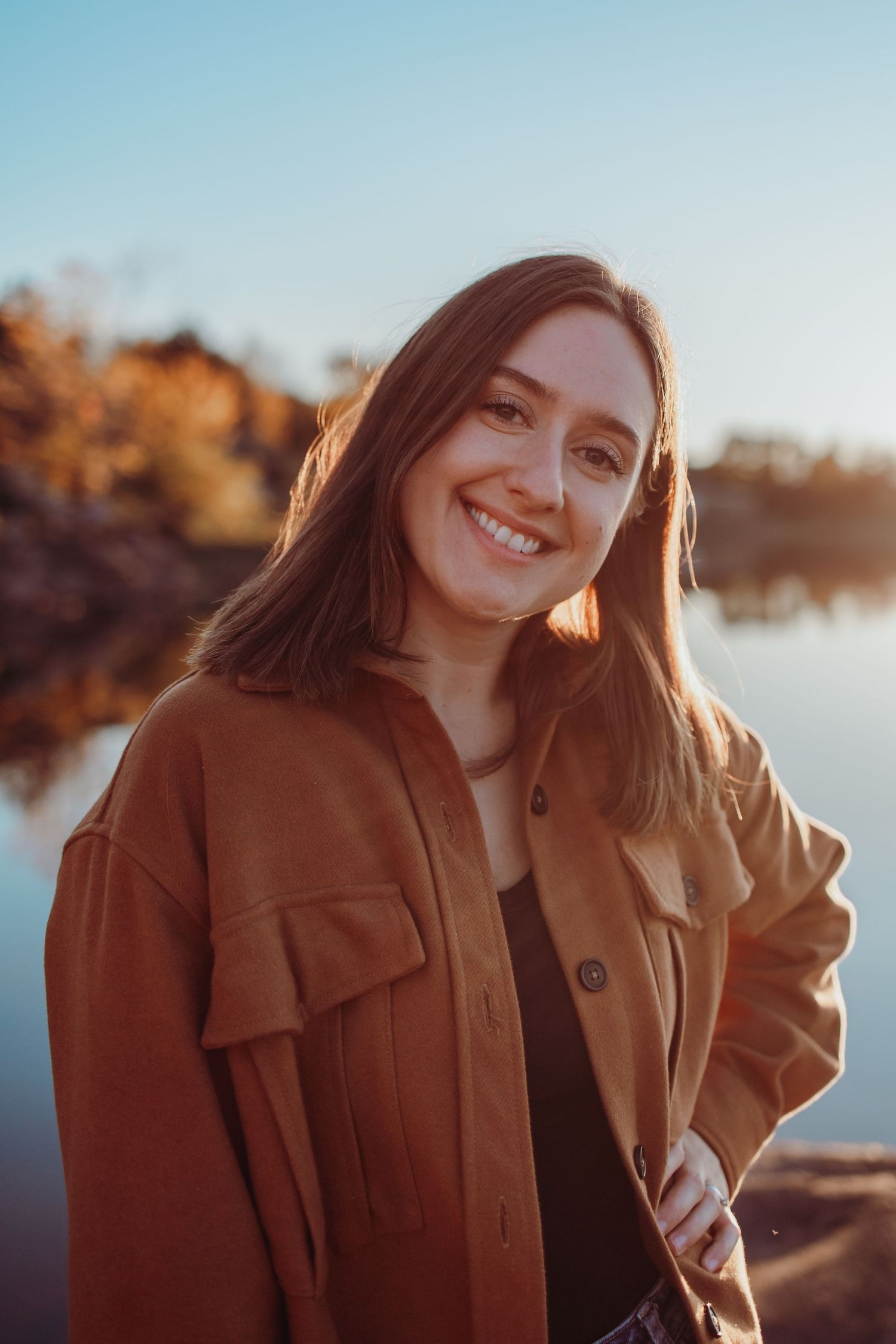 Portrait series of someone in a brown coat smiling warmly during golden hour by a lake.