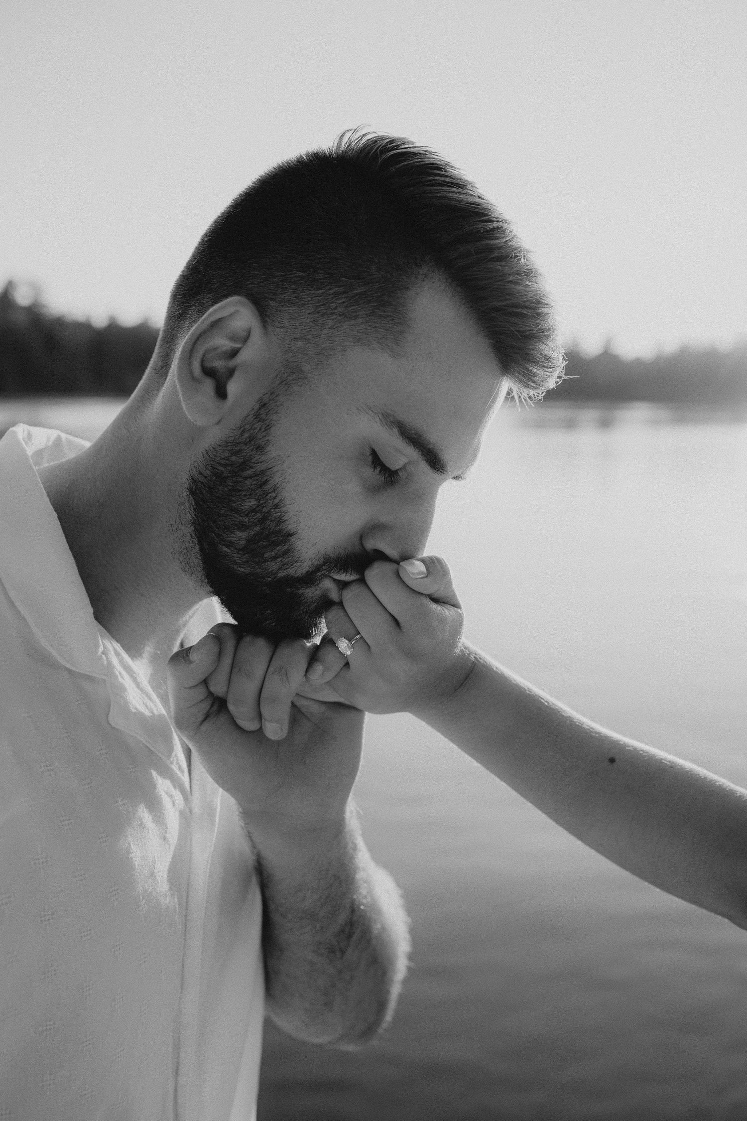 Intimate black and white photo of a tender moment during a romantic gesture by a lakeside.