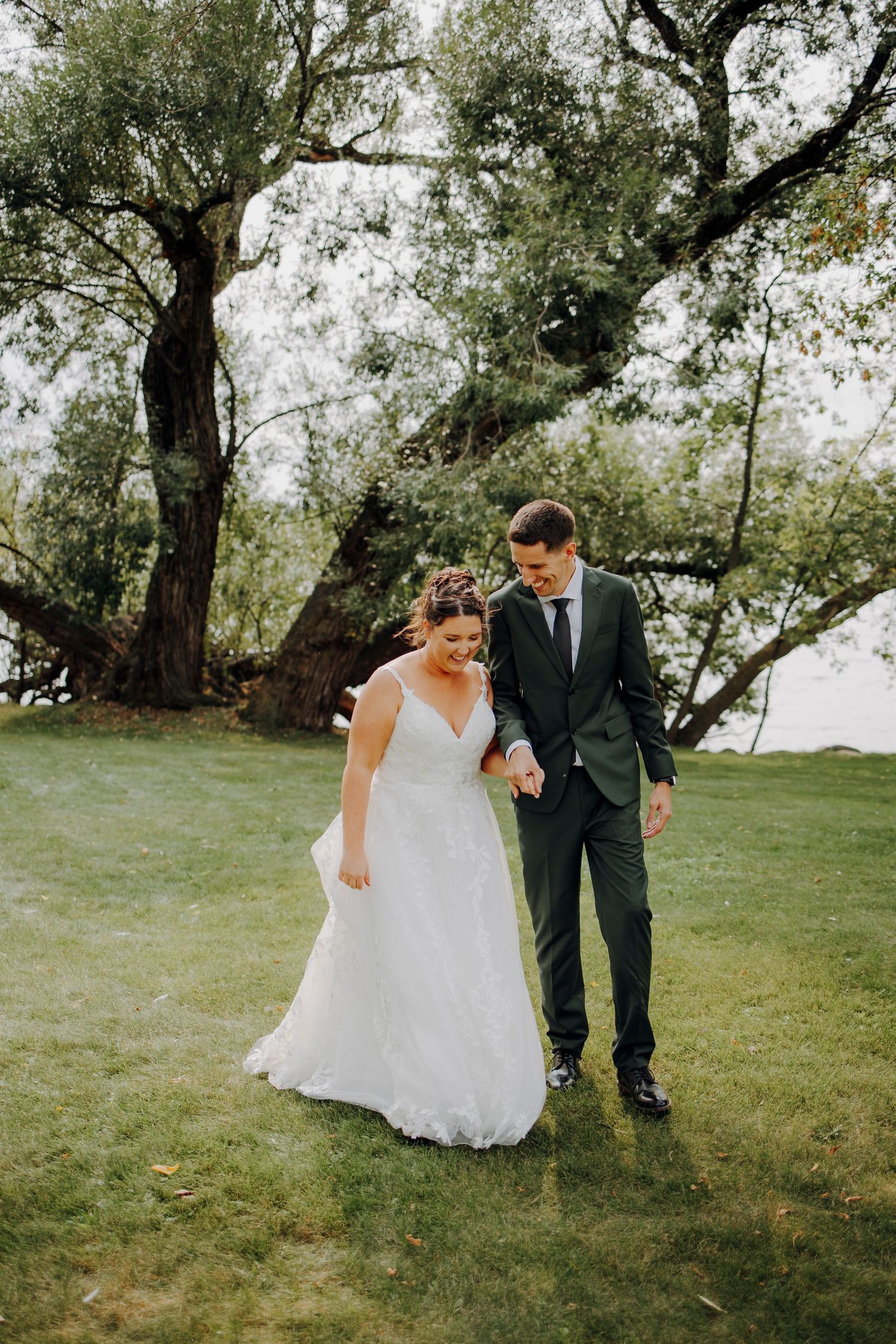 Newlyweds walking hand in hand through lush green garden setting.