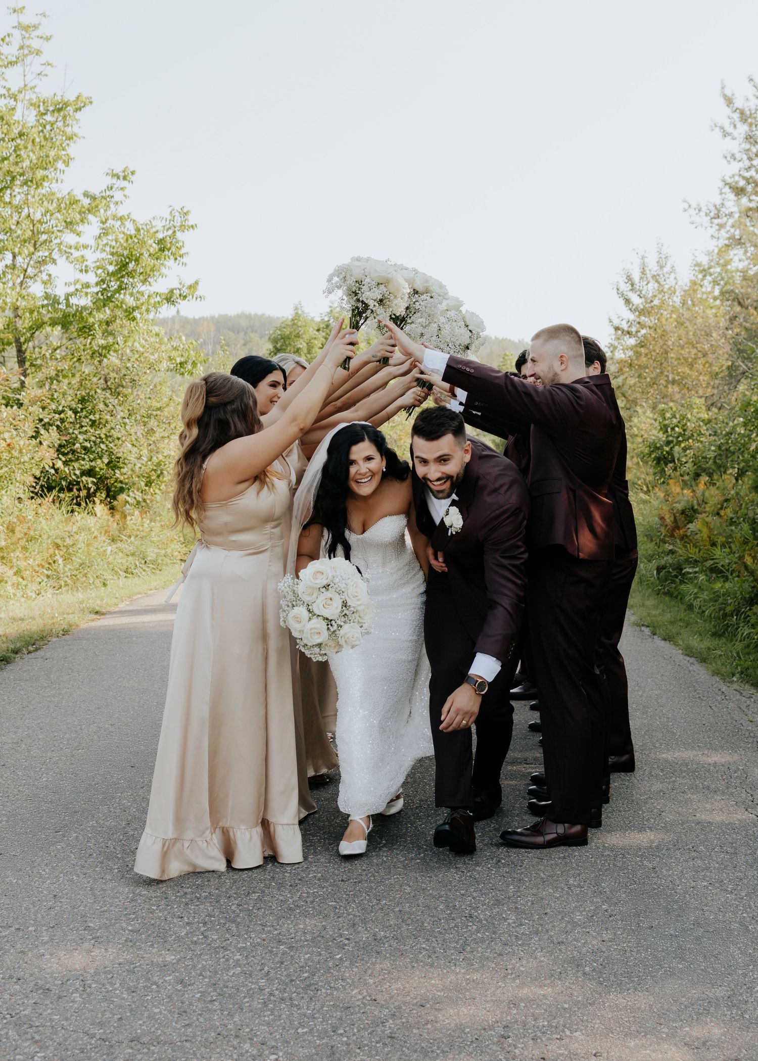 Wedding party members pose together on a path outdoors in coordinated formal attire.