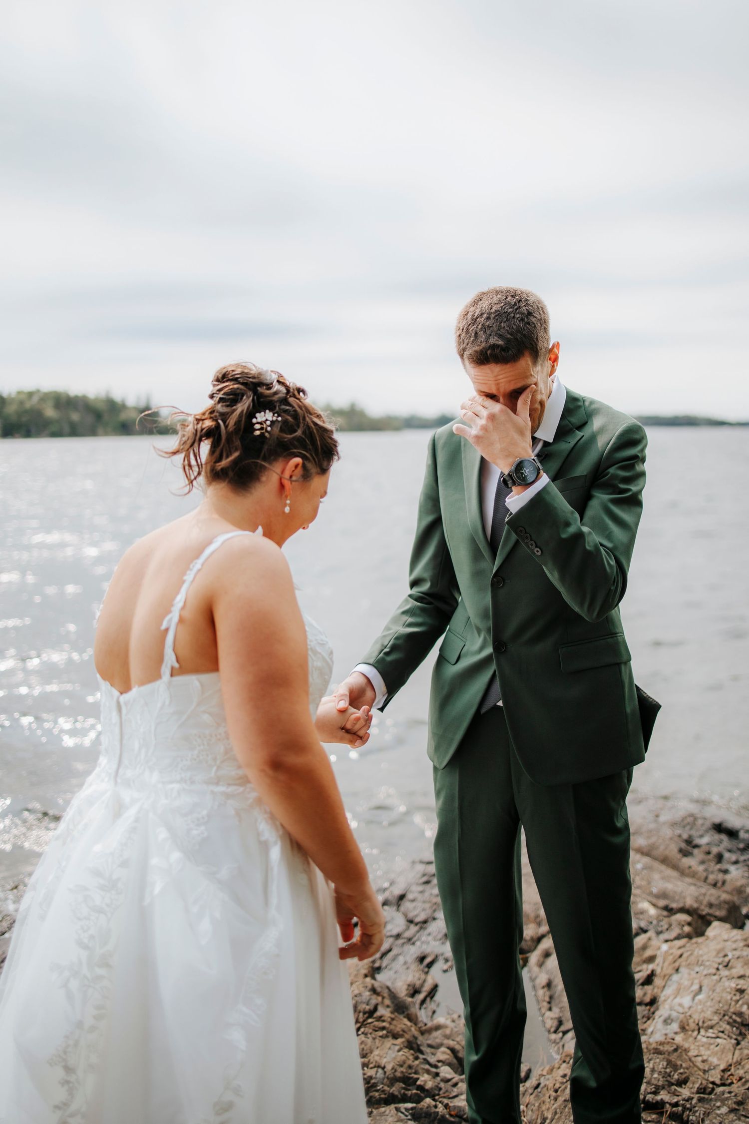 Emotional wedding moment captured between couple on rocky shoreline.