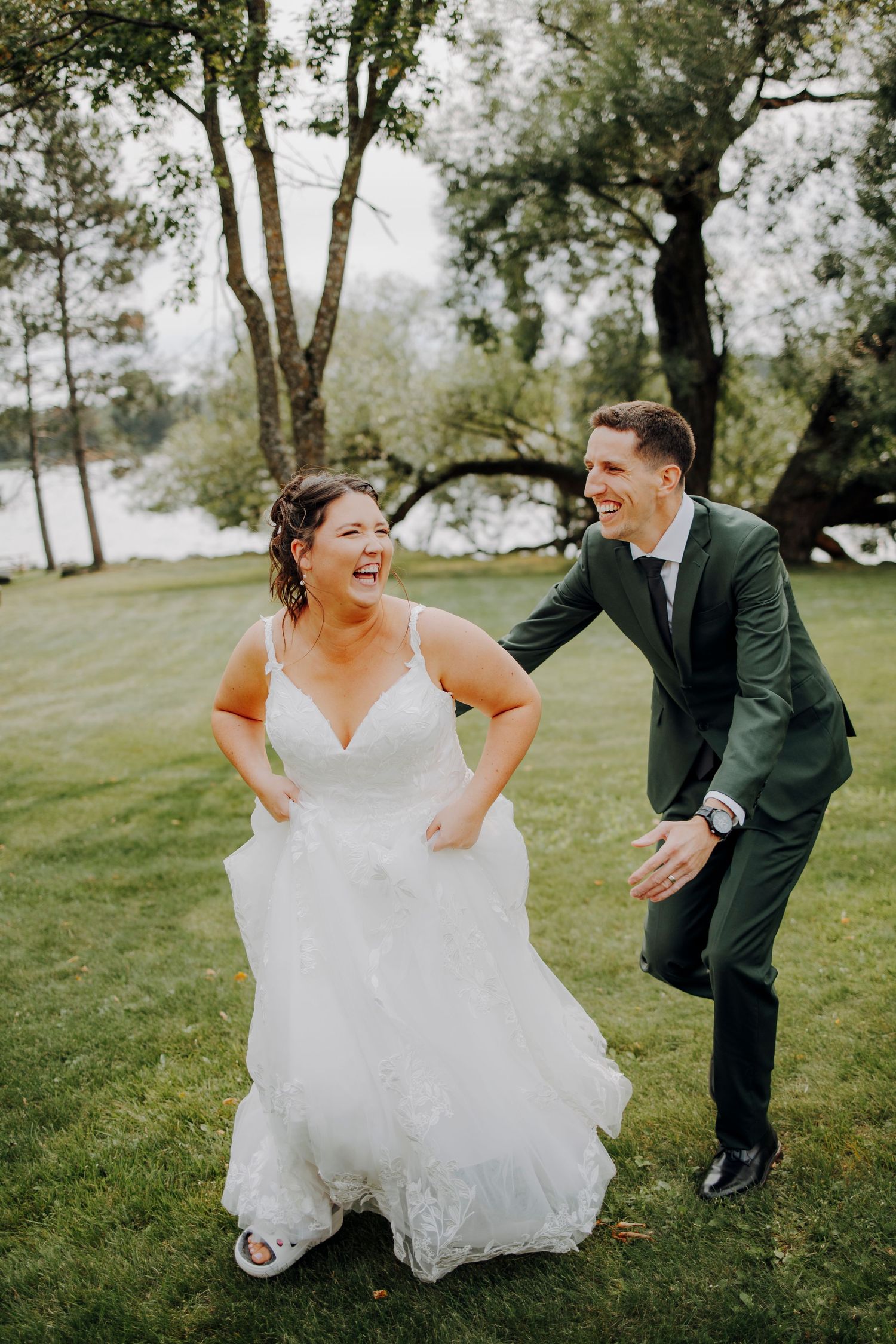 Playful wedding couple laughs together on grassy lawn during outdoor photo session.