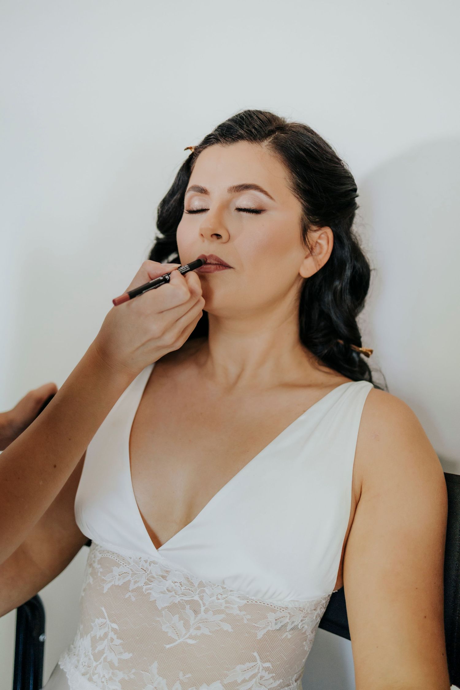 Makeup artist applying cosmetics to someone wearing a white lace dress.