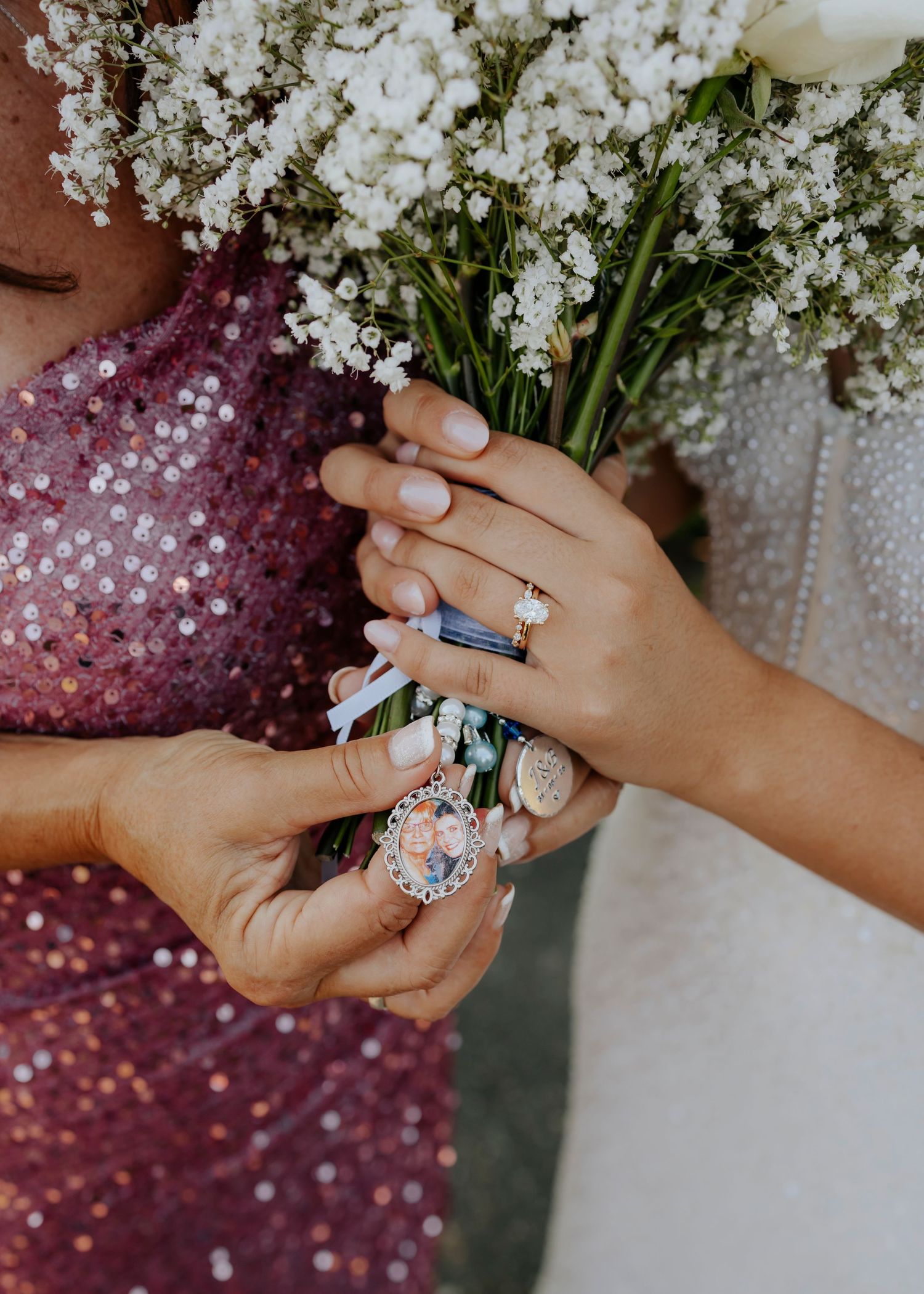 Hands holding white flowers show off wedding rings and sparkly burgundy dress details.