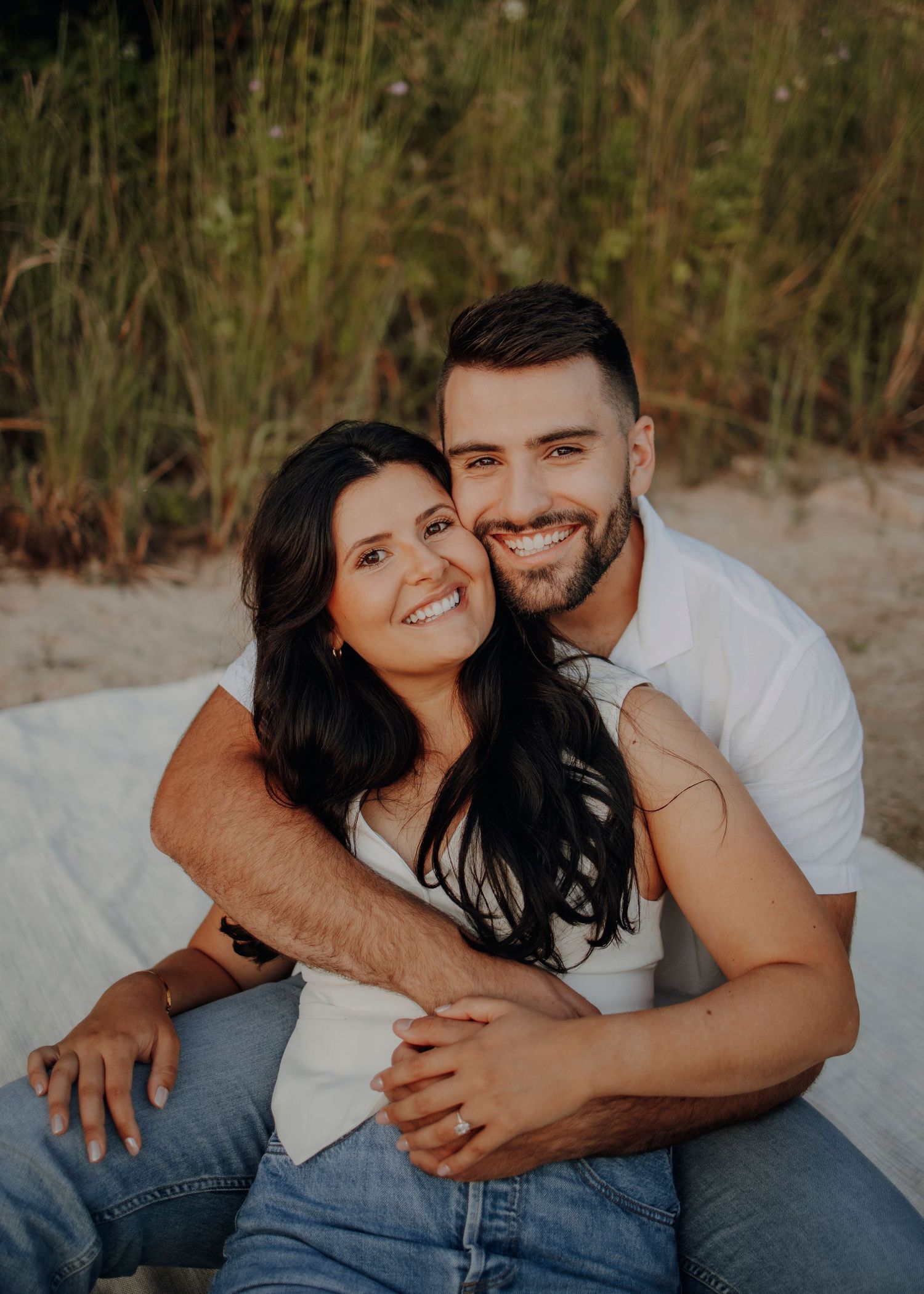 Couple in casual attire sharing loving embrace on sandy beach.