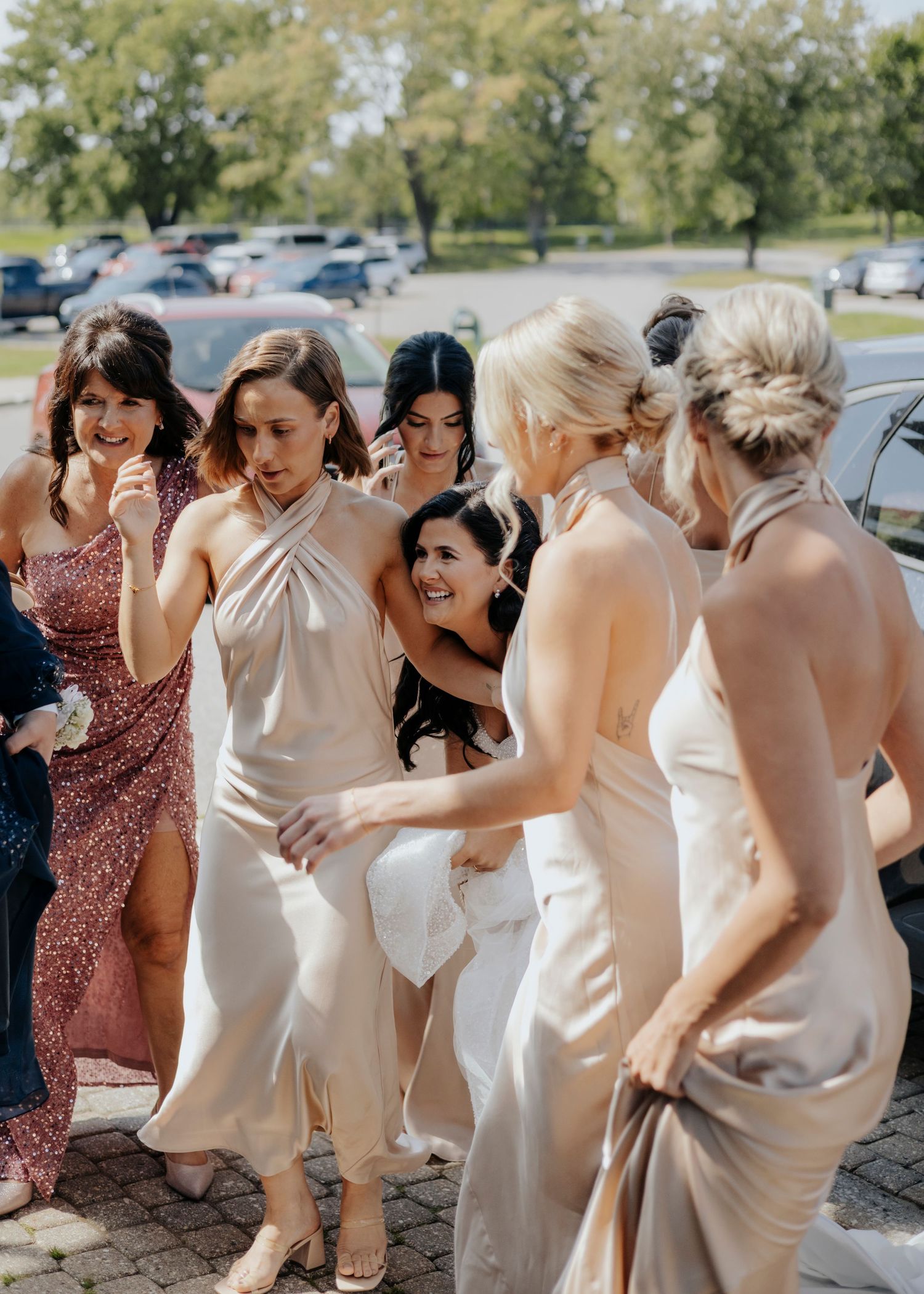 Wedding party members in light colored dresses dance together at an outdoor celebration.