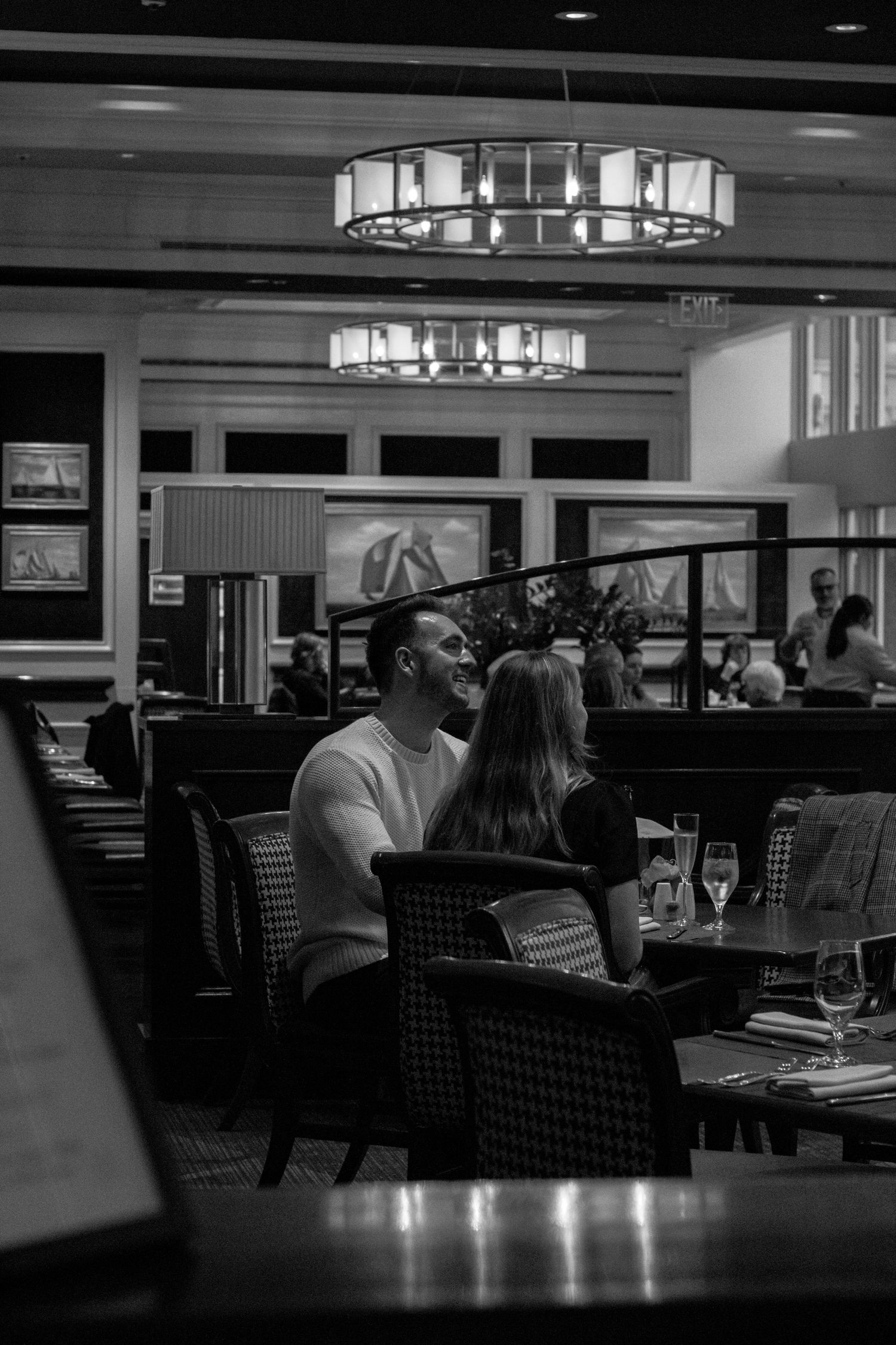 Couple sharing romantic moment at elegant restaurant with chandelier lighting in black and white.