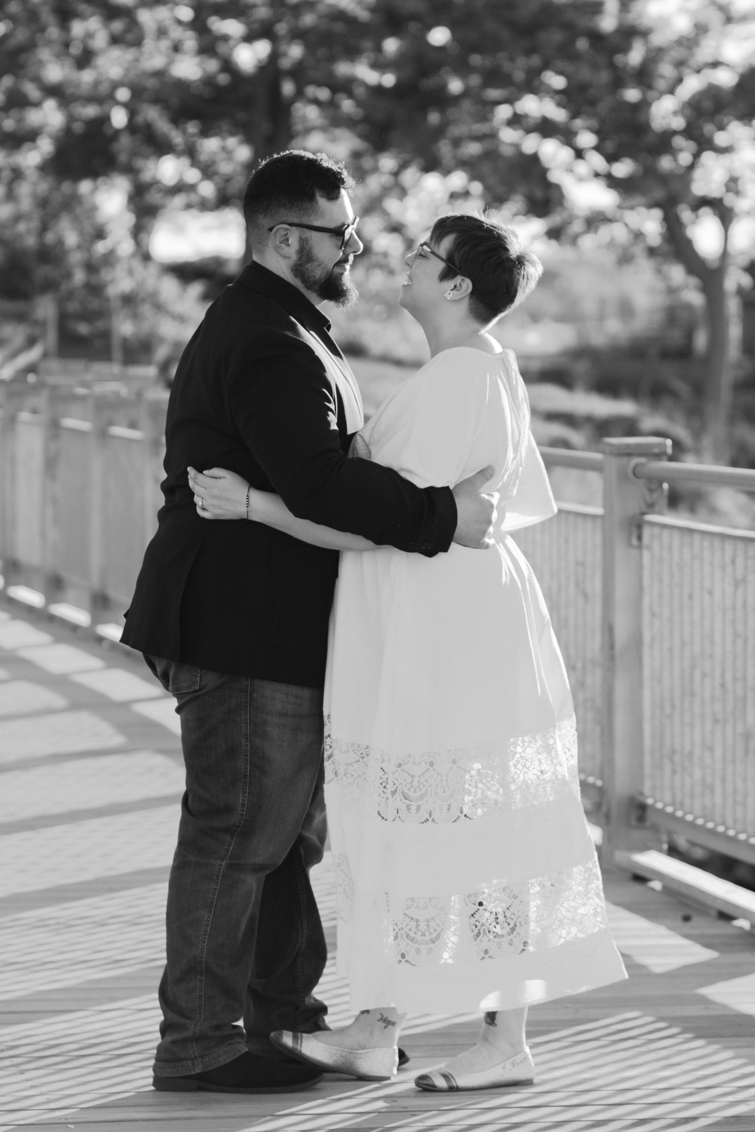 Black and white photo of a couple sharing a kiss on a wooden bridge outdoors.