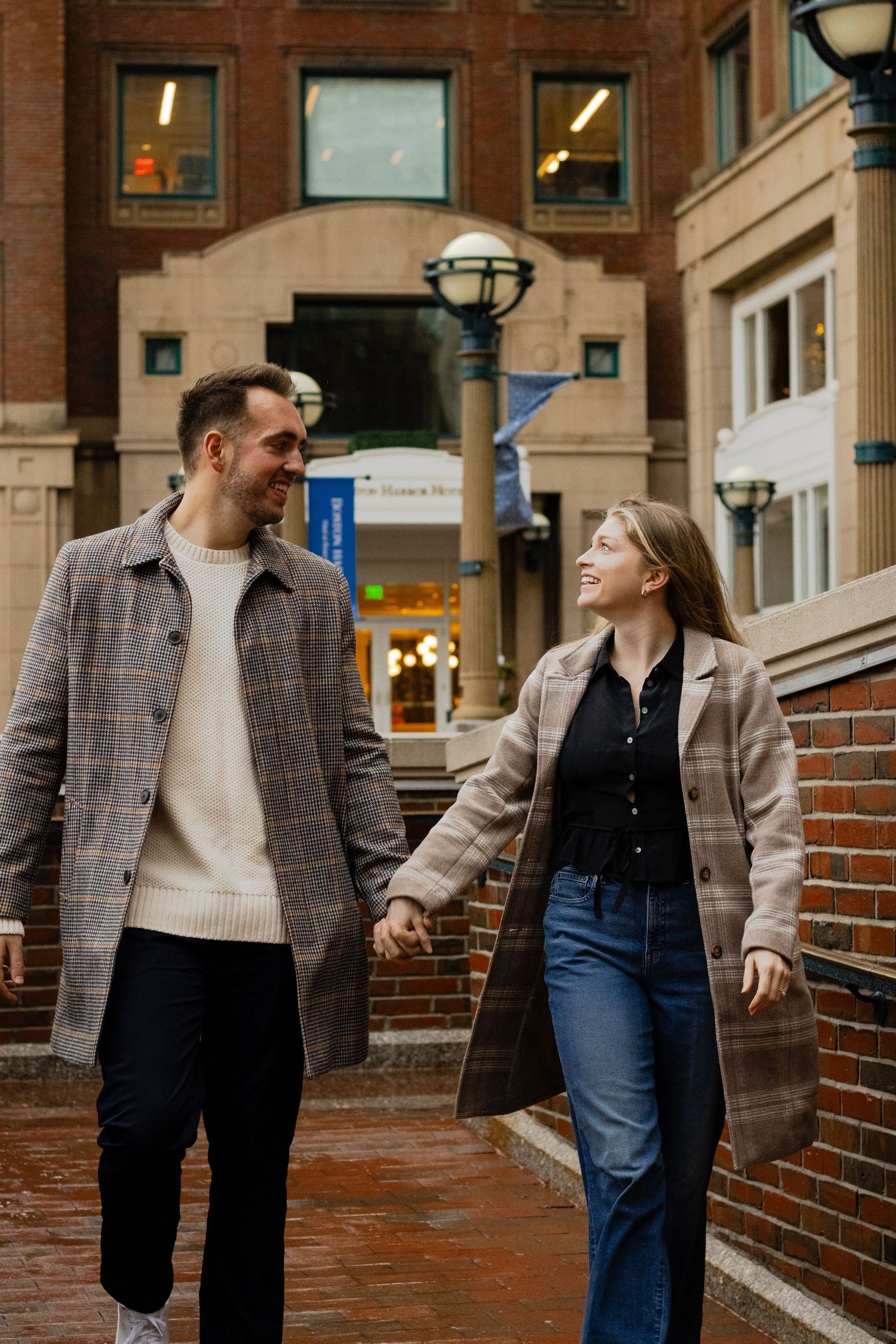 A happy couple holds hands and smiles while walking through a brick urban plaza together.