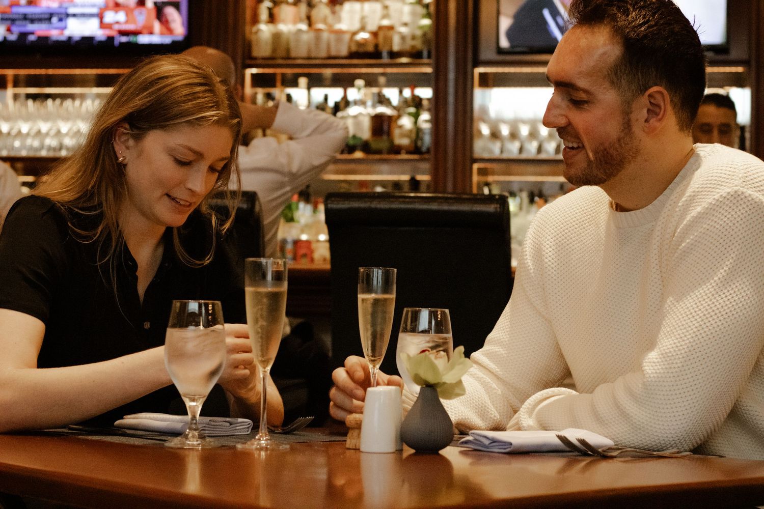 Couple enjoying champagne together at a restaurant bar, smiling and celebrating their engagement.