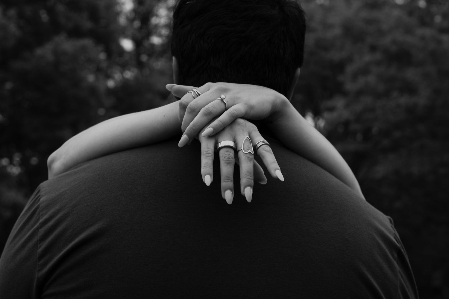 Black and white photo of a couple embracing, woman's hand with rings resting on man's shoulder.
