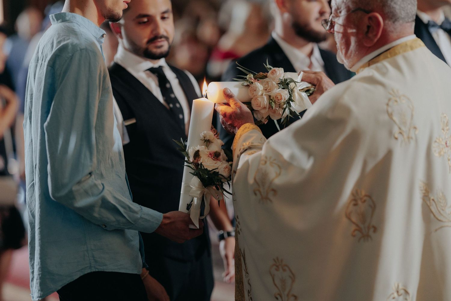 Preot aprinzând lumânările de cununie decorate cu flori în timpul slujbei religioase; moment solemn surprins în detaliu în biserică.