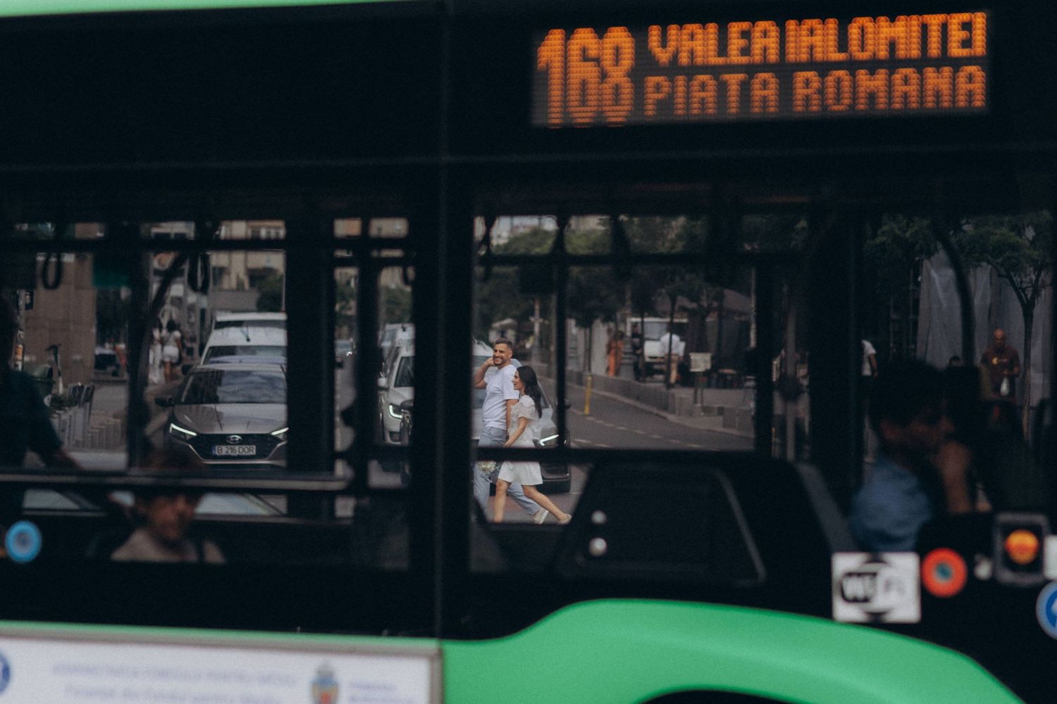 Andreea și Vlad traversând strada, surprinși prin geamul unui autobuz 168; cadru urban creativ în București.