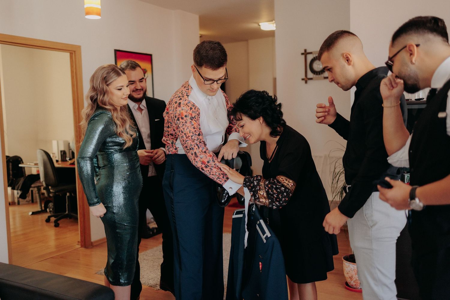 Mirele ajutat de mamă și prieteni să își pună uniforma militară; moment emoționant de familie surprins în timpul pregătirilor de nuntă.