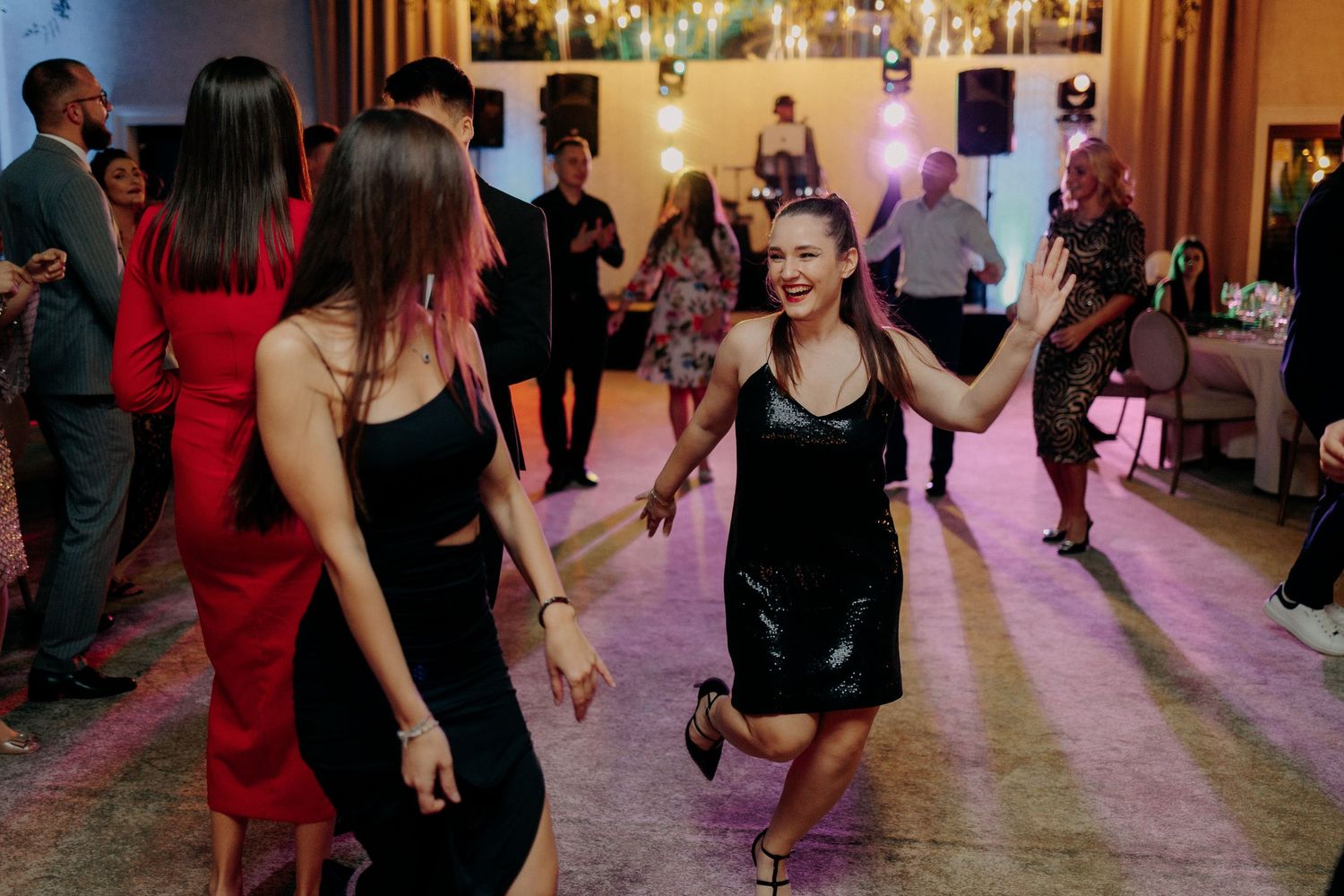 Invitată zâmbind și dansând cu entuziasm la petrecerea de nuntă; atmosferă plină de viață pe ringul de dans, într-un decor festiv cu lumini.
