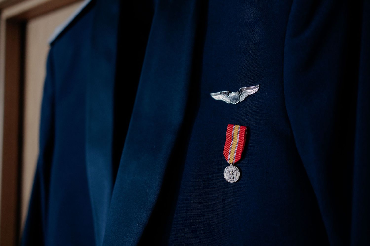 Plan detaliu cu haina militară de gală a mirelui, decorată cu aripi de pilot și o medalie cu panglică roșie; accesorii oficiale pentru nuntă