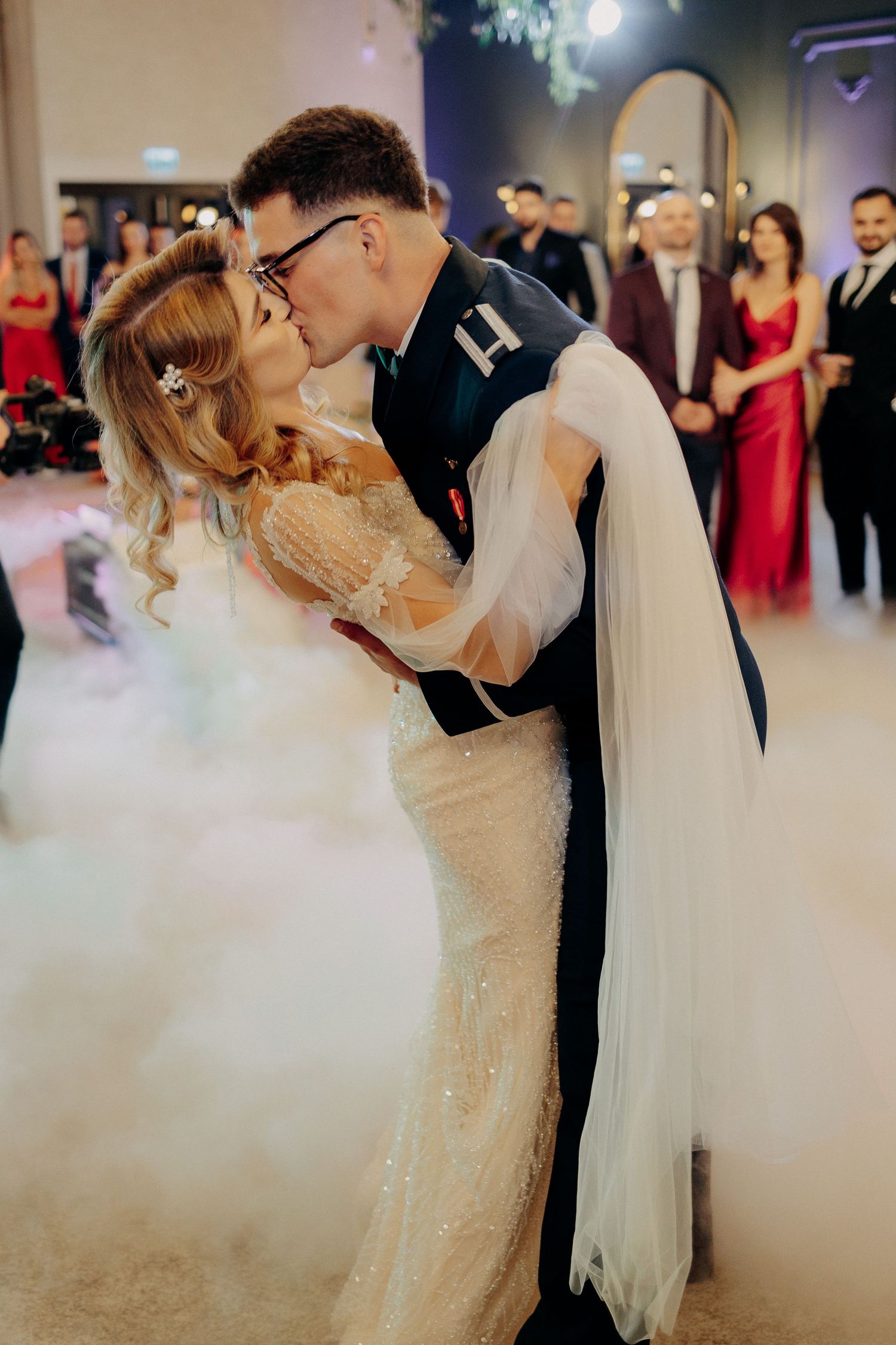 Miri sărutându-se pasional pe ringul de dans, înconjurați de un nor de fum alb; moment romantic și spectaculos la o nuntă elegantă.