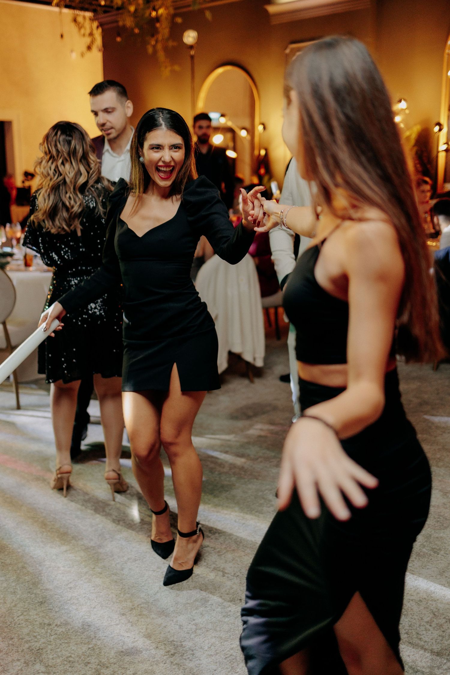 Invitată în rochie neagră scurtă dansând plină de voie bună; atmosferă efervescentă pe ringul de dans la o petrecere de nuntă modernă.