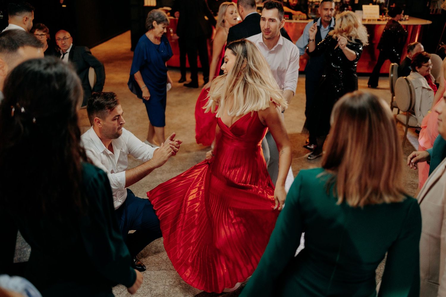 Invitată în rochie roșie lungă dansând cu energie; moment dinamic pe ringul de dans la o petrecere de nuntă elegantă.