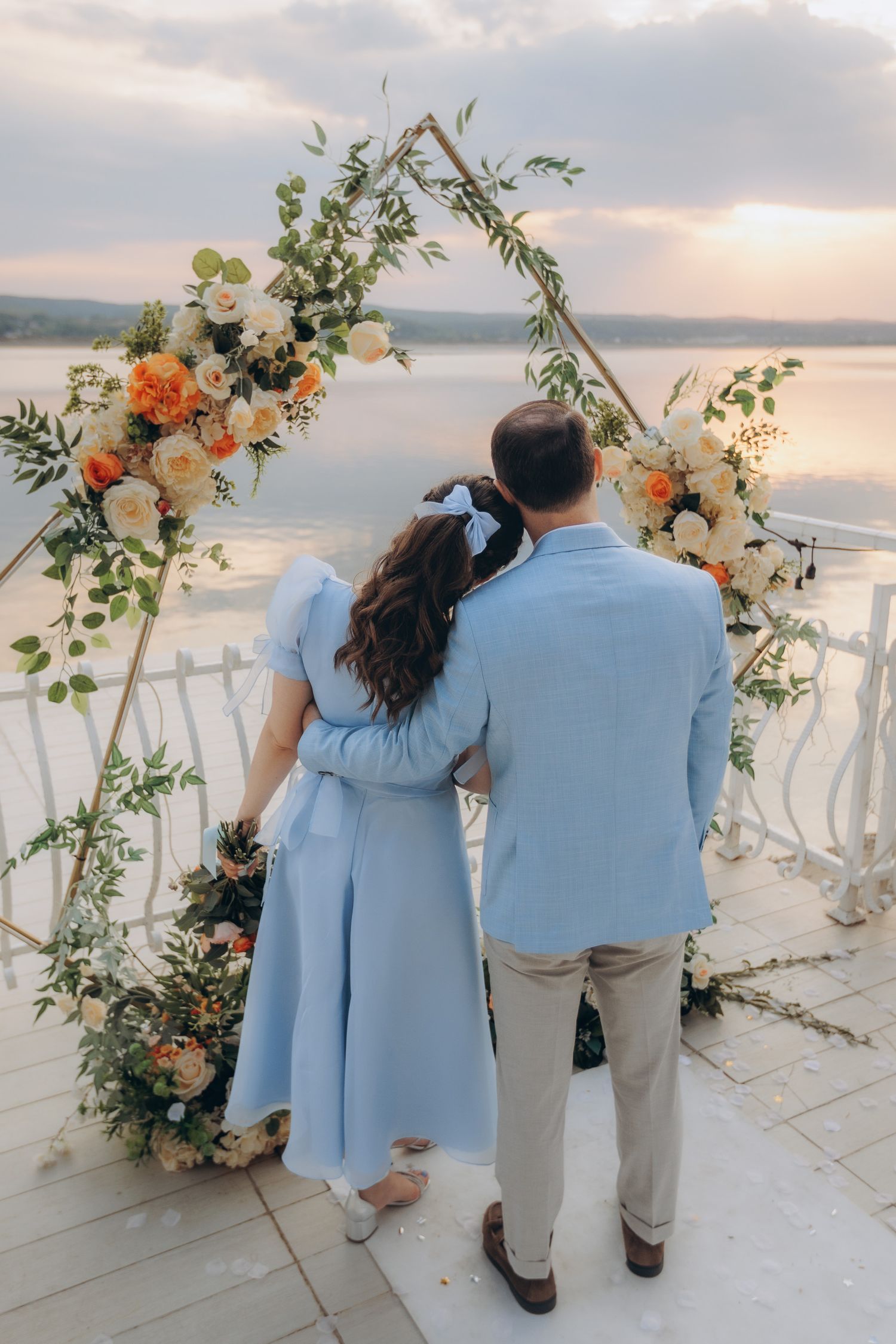 Portret de cuplu la cununia civilă pe malul lacului Budeasa, sub o arcadă cu flori naturale, într-un decor romantic la apus de soare.
