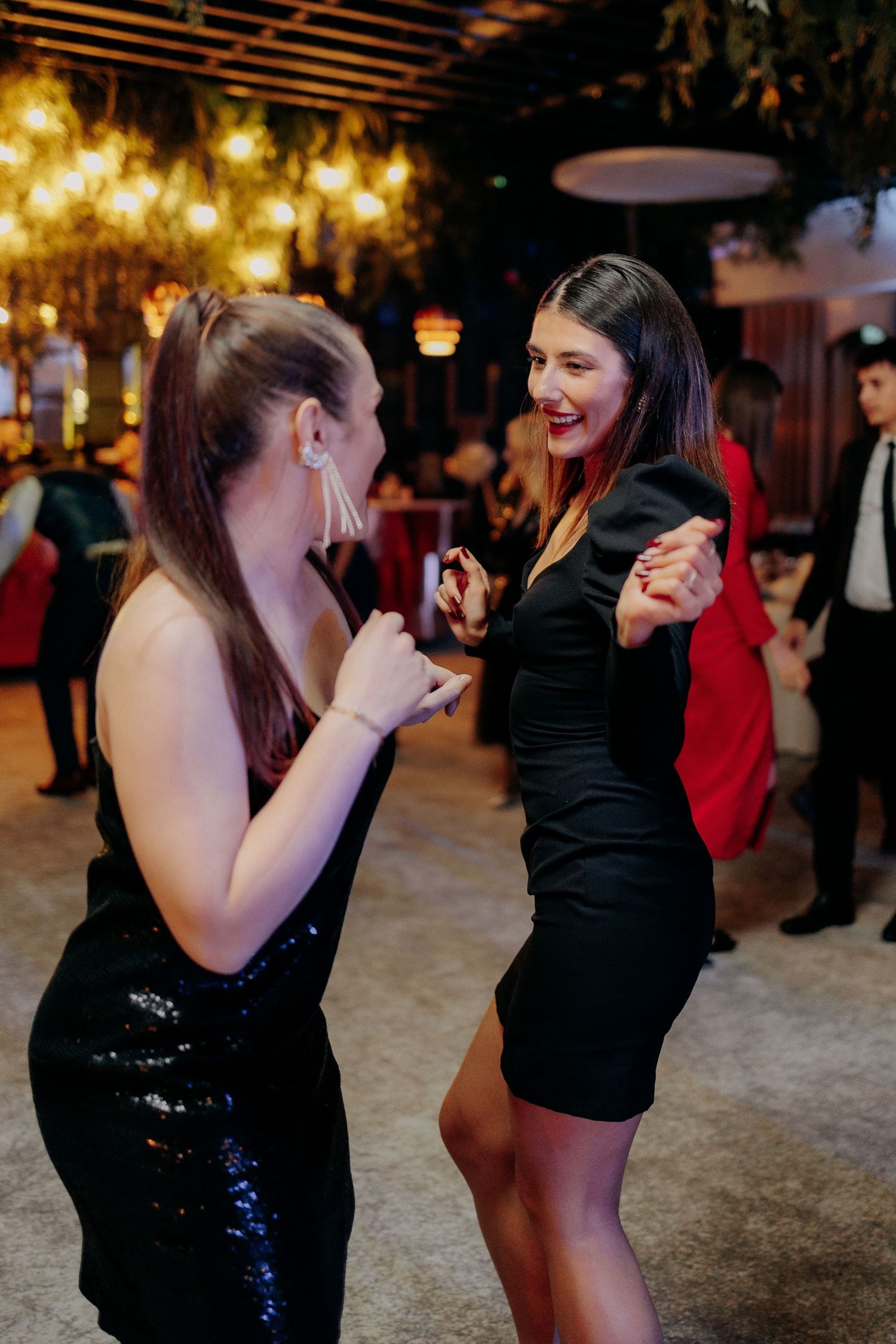 Două invitate în rochii negre elegante dansând și zâmbind; atmosferă veselă și plină de complicitate pe ringul de dans la o nuntă.