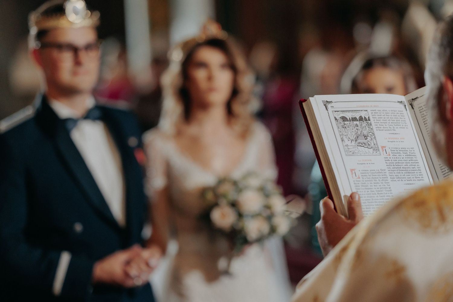 Plan apropiat cu Biblia deschisă în timpul cununiei religioase; mirii sunt vizibili în fundal, purtând coroane, într-un cadru de poveste.