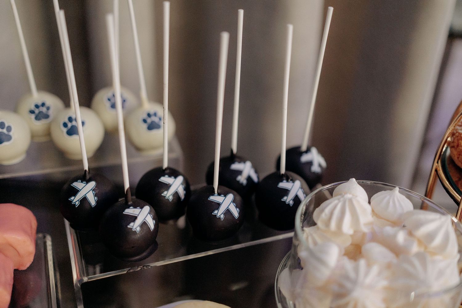 Cake pops de ciocolată decorate cu avioane albe și bezele crocante; detalii tematice creative la candy bar-ul unei nunți elegante.