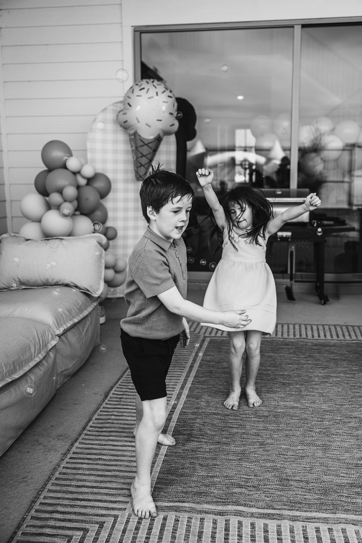 Two barefoot children dancing and playing at a festive party with balloon decorations in black and white photo.