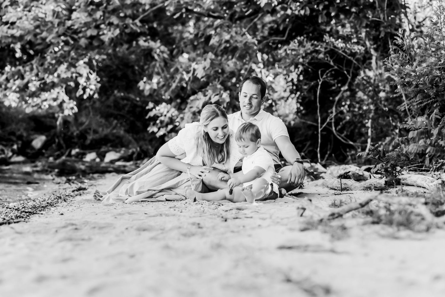 Black and white portrait of wedding party lounging casually on grass under trees.
