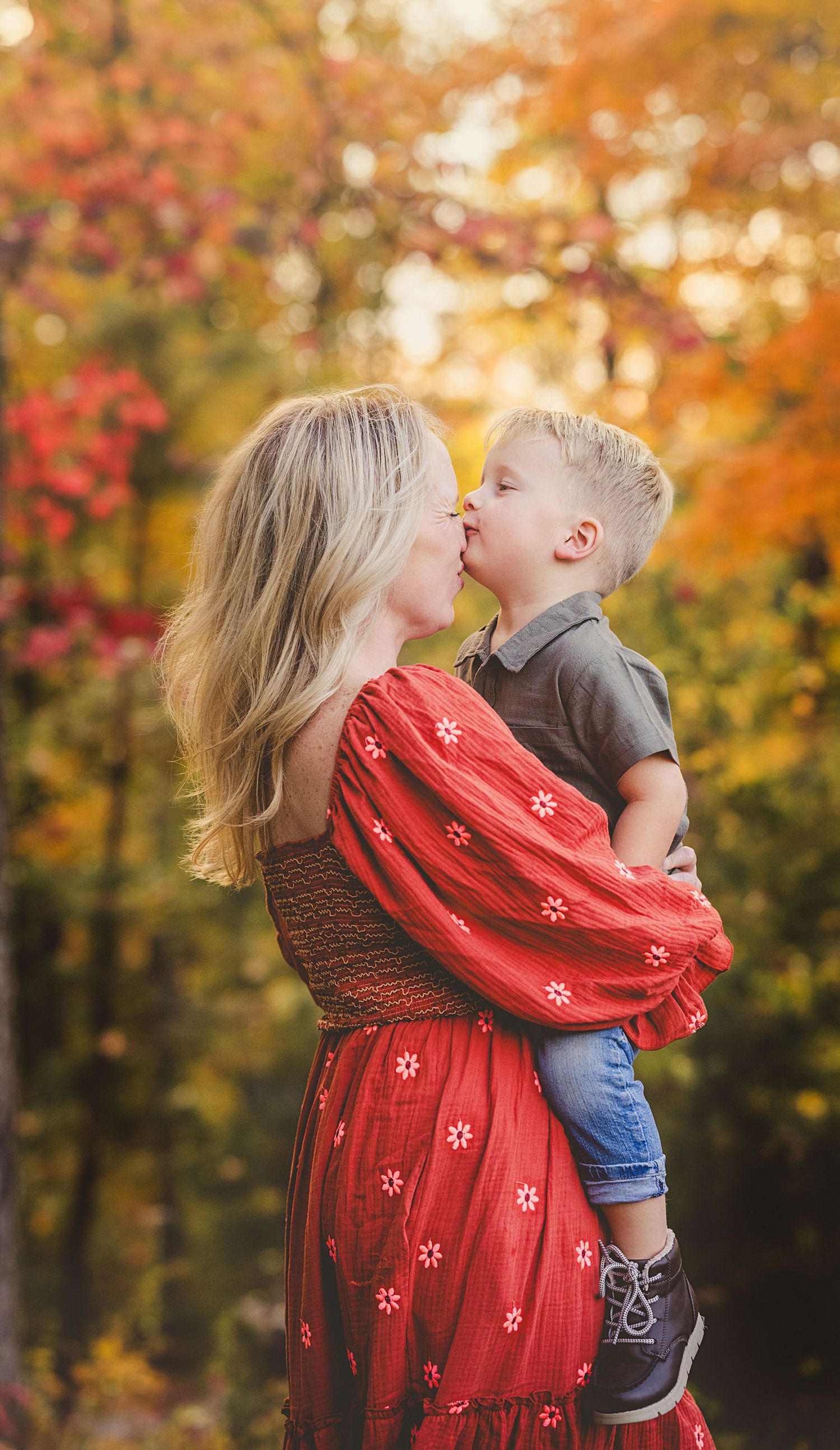 A tender moment captured against vibrant fall foliage with a red scarf flowing in the breeze.