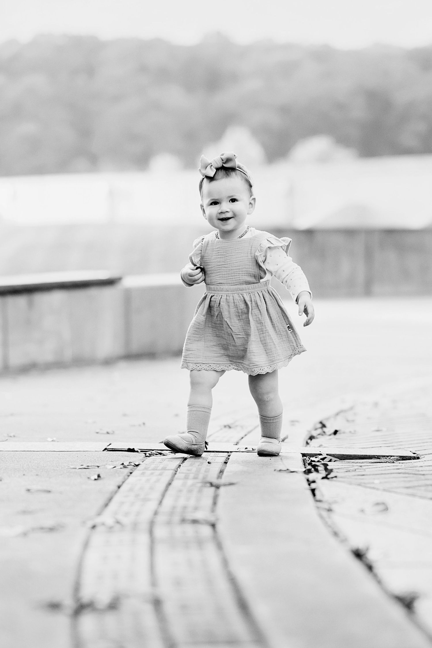 Black and white sequence of a toddler walking across wooden boards in casual clothing.
