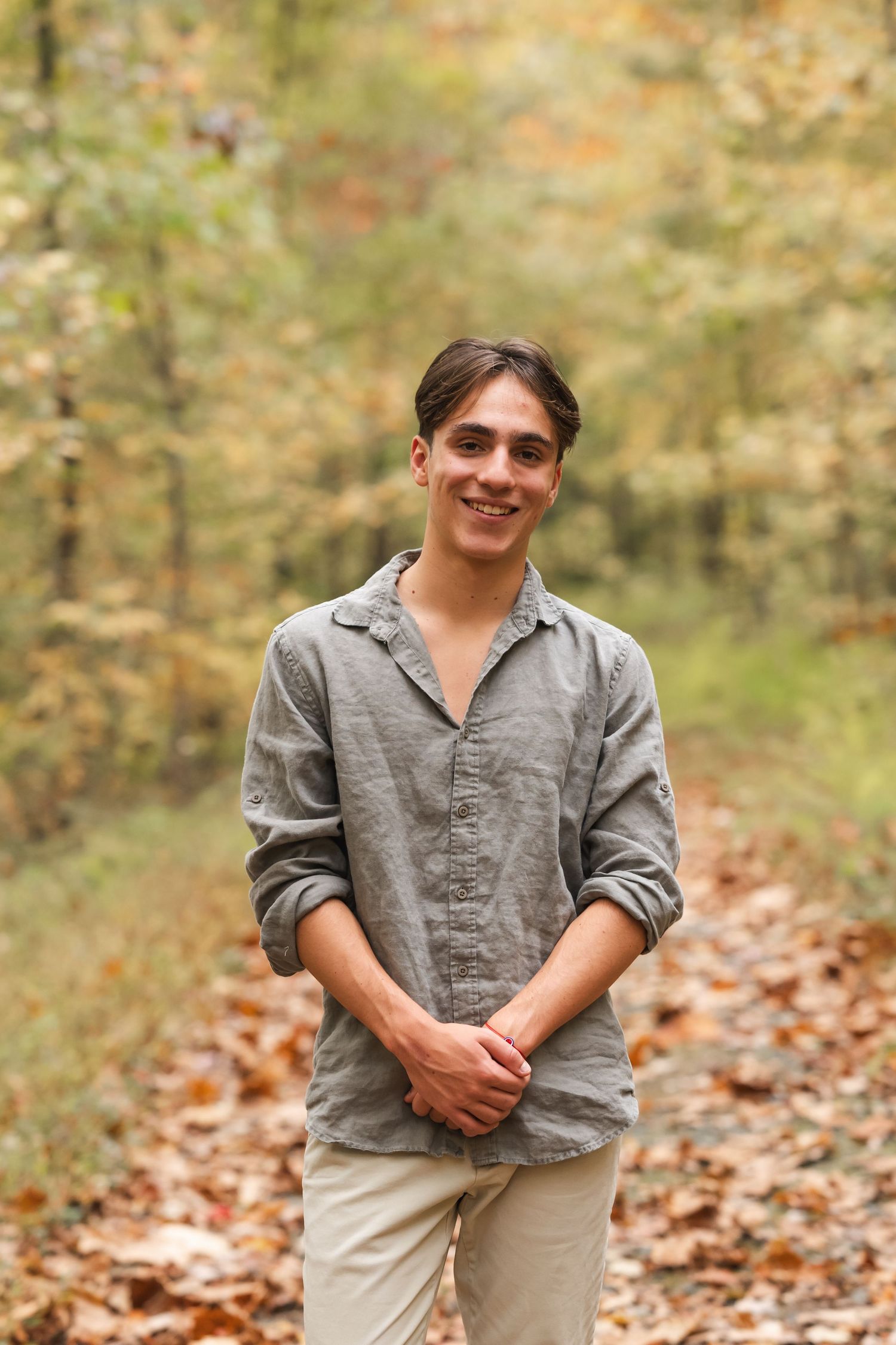Young person in casual grey shirt poses in autumn forest setting.