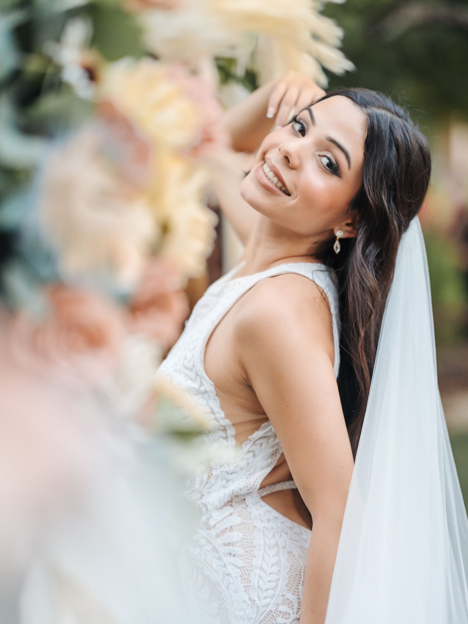 A bride smiles joyfully in golden natural lighting while wearing a white lace gown and flowing veil.